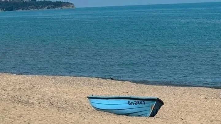 Small blue boat resting on a sandy beach beside calm sea water on a clear day.