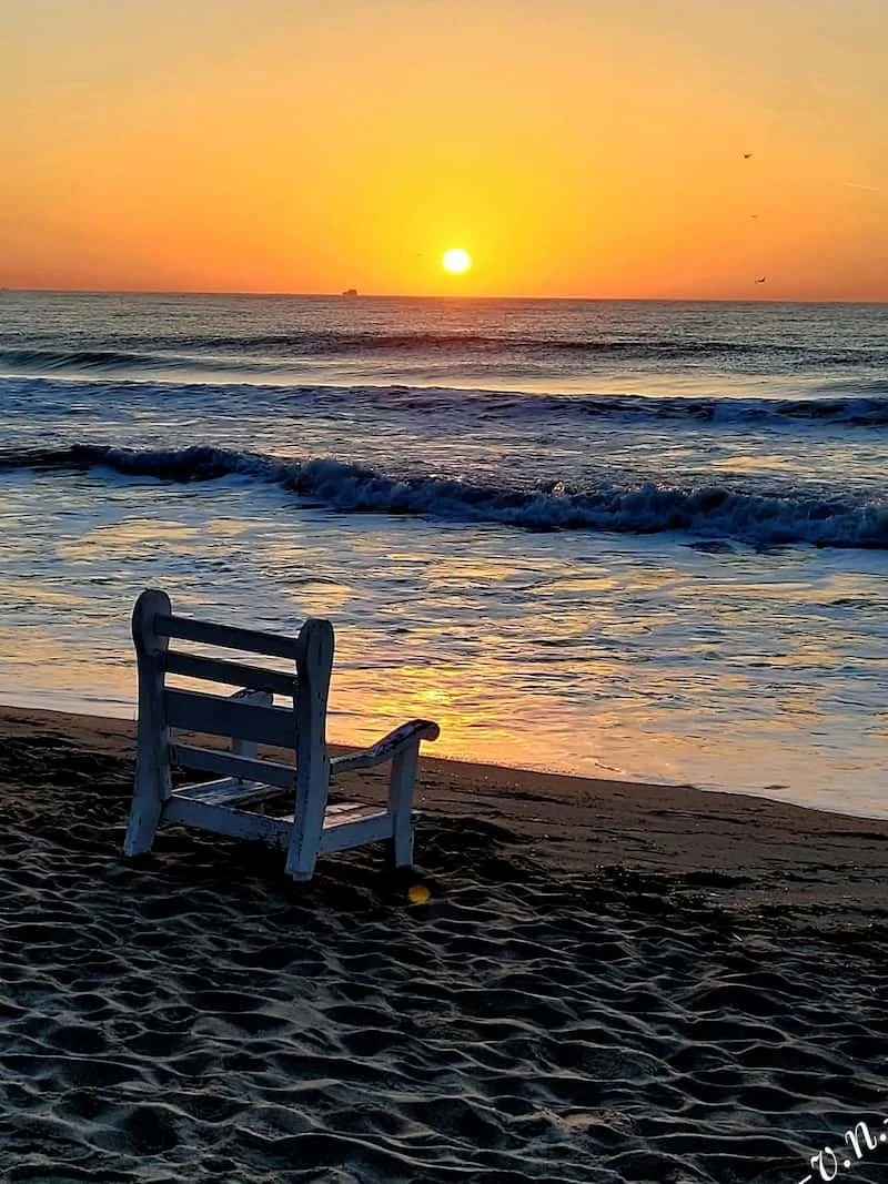 Sunrise over a quiet beach with an empty chair, symbolizing reflection, self-discovery, and the beginning of a healing journey.