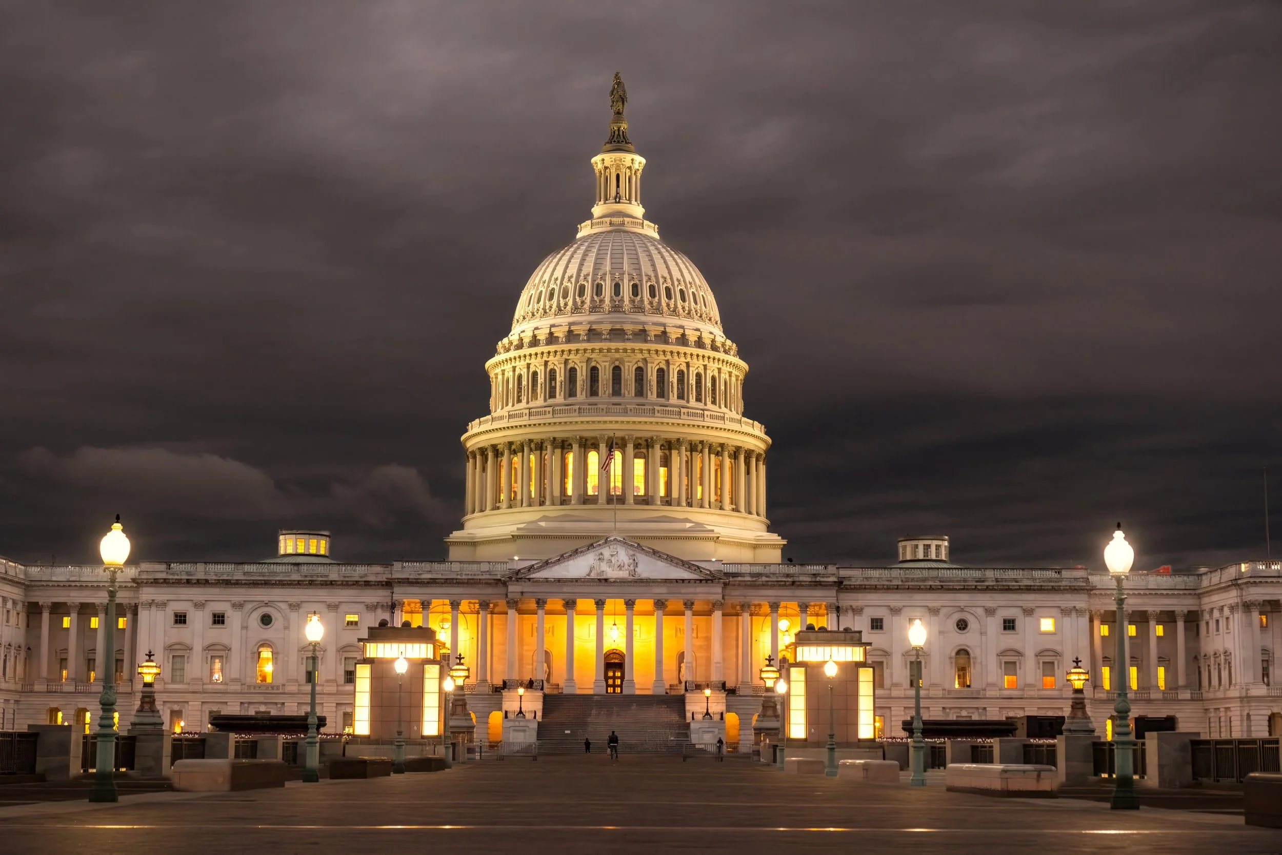The United States Capitol building illuminated at night with a dark, cloudy sky in the background.