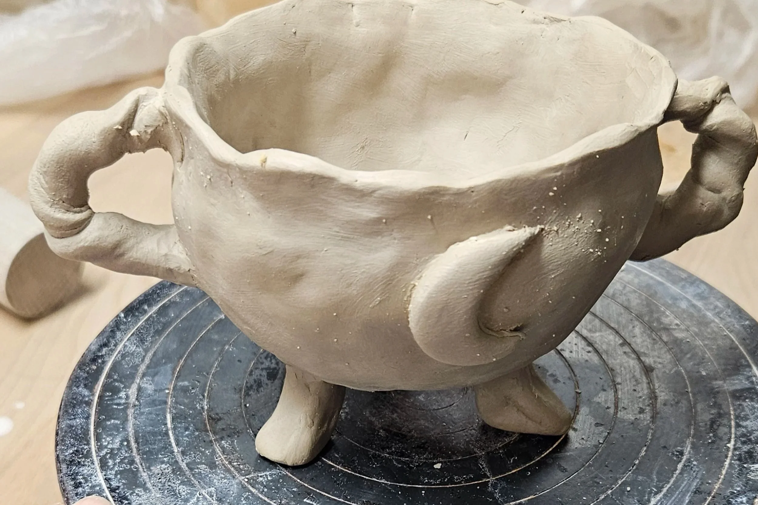 Une sculpture en argile en forme de bol avec deux petites anses, posée sur un plateau tournant, en cours de fabrication.