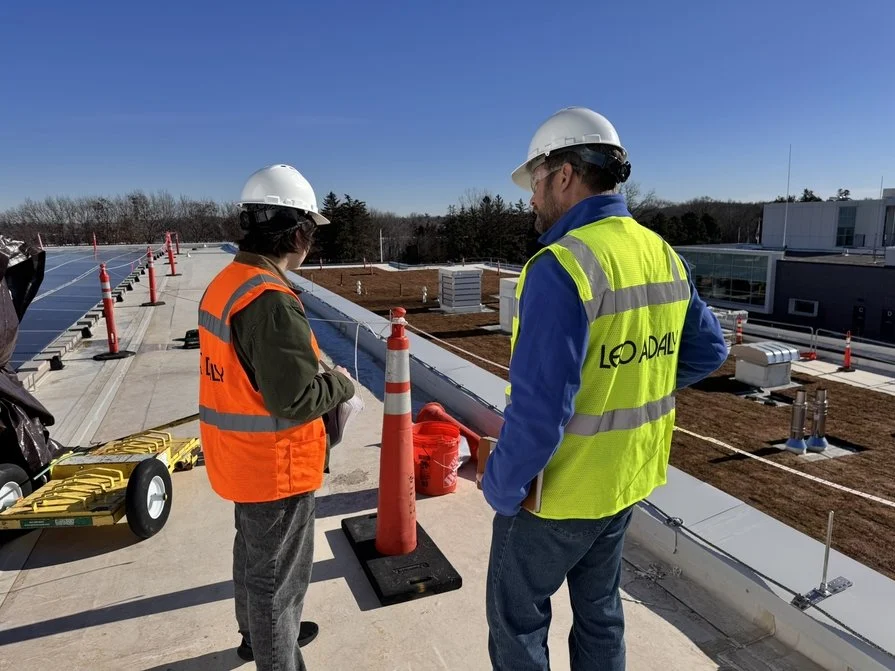 LEO A DALY project team members on the roof of Hennepin County Sheriff Office Public Safety Headquarters during construction reviewing work in progress. Both men wearing construction hard hats and reflective vests branded LEO A DALY on the back.