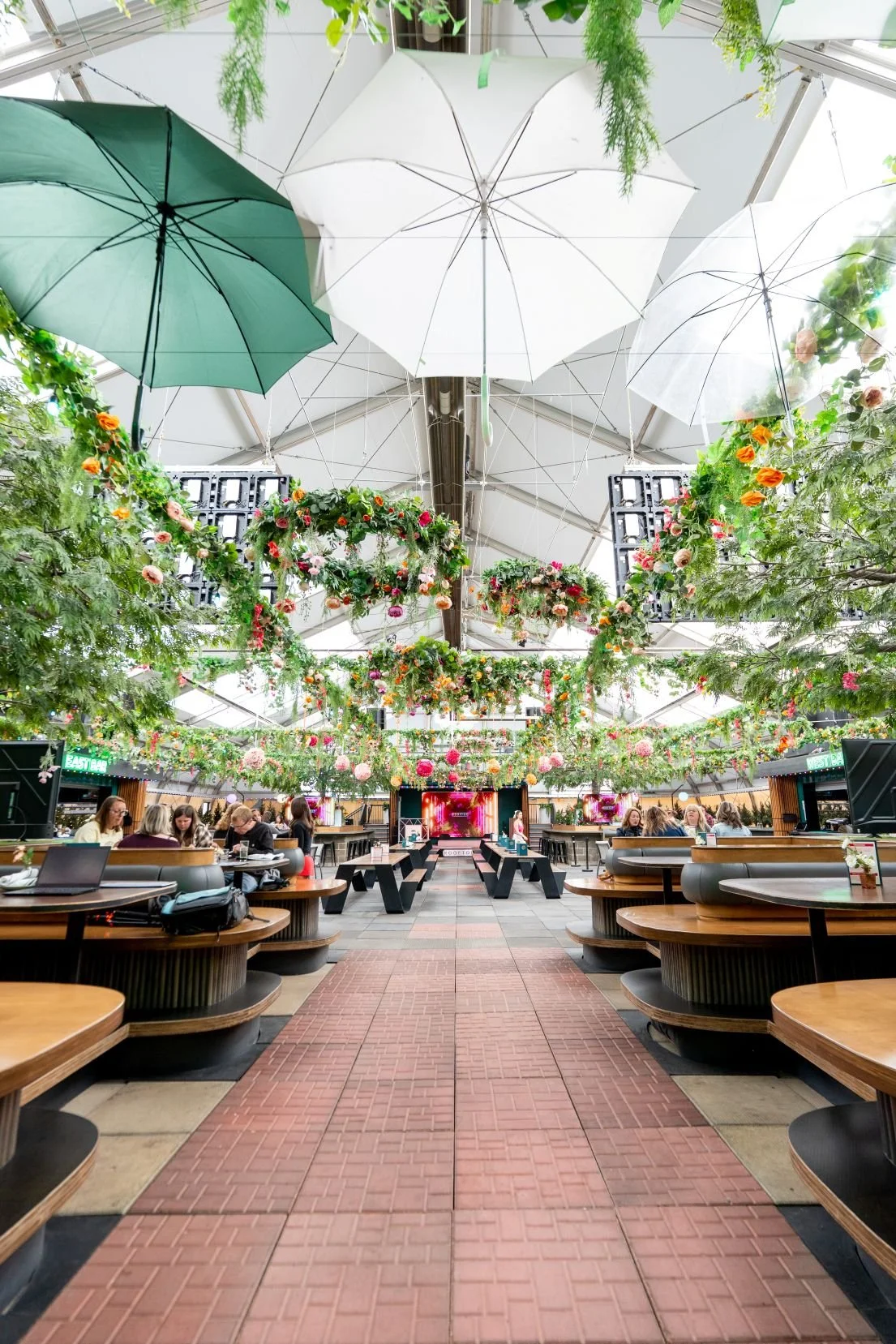 An elegant indoor event venue featuring hanging green umbrellas and floral wreaths captured by Aces and Oak.