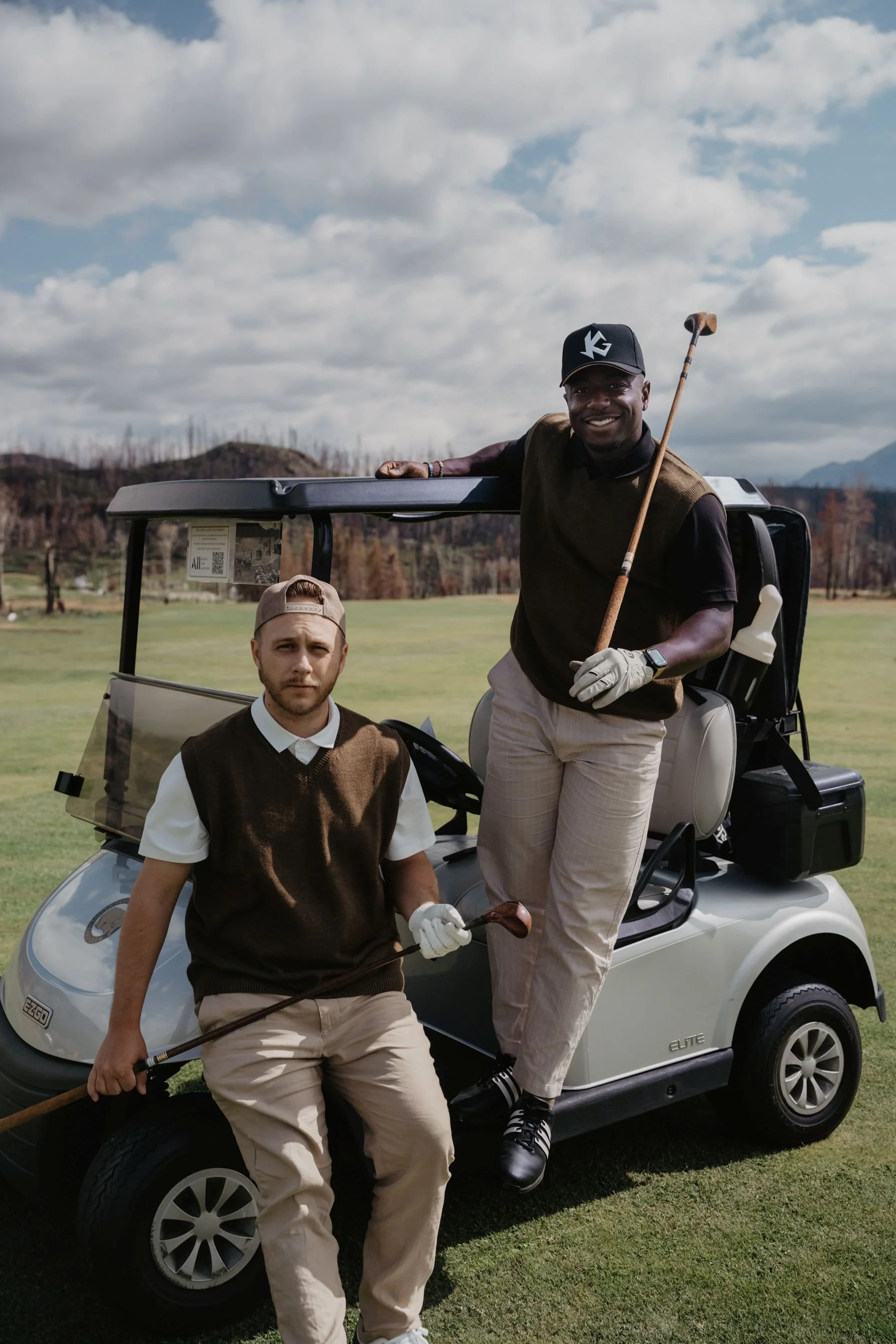 Two men wearing golf apparel posing next to a golf cart during a commercial lifestyle shoot by Aces and Oak.