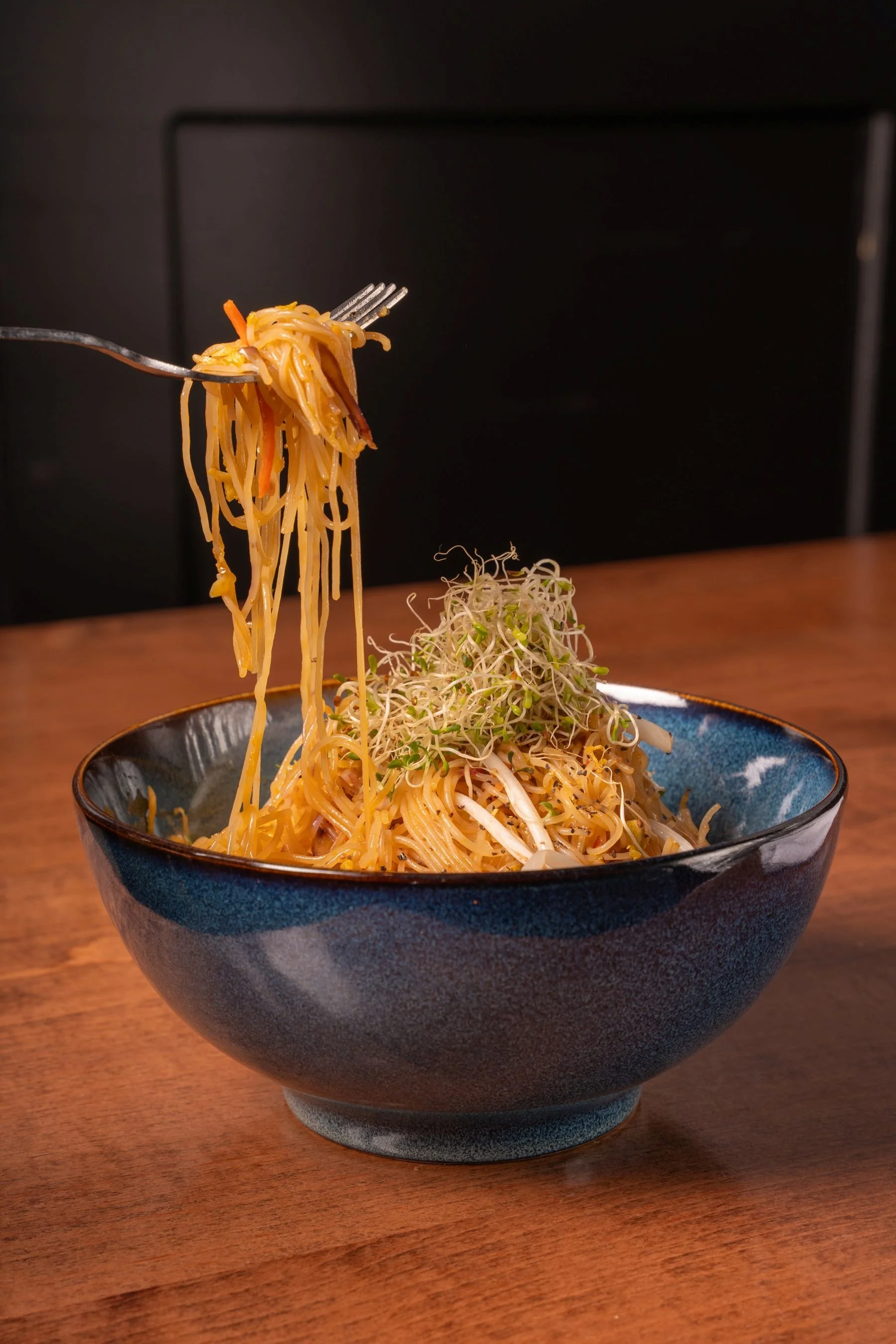 A close-up of noodles being lifted with chopsticks from a steaming bowl during a restaurant commercial shoot.