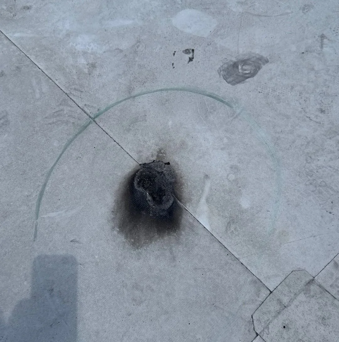 Burnt or charred object on a concrete floor, with burn marks and a clear circular line surrounding it.