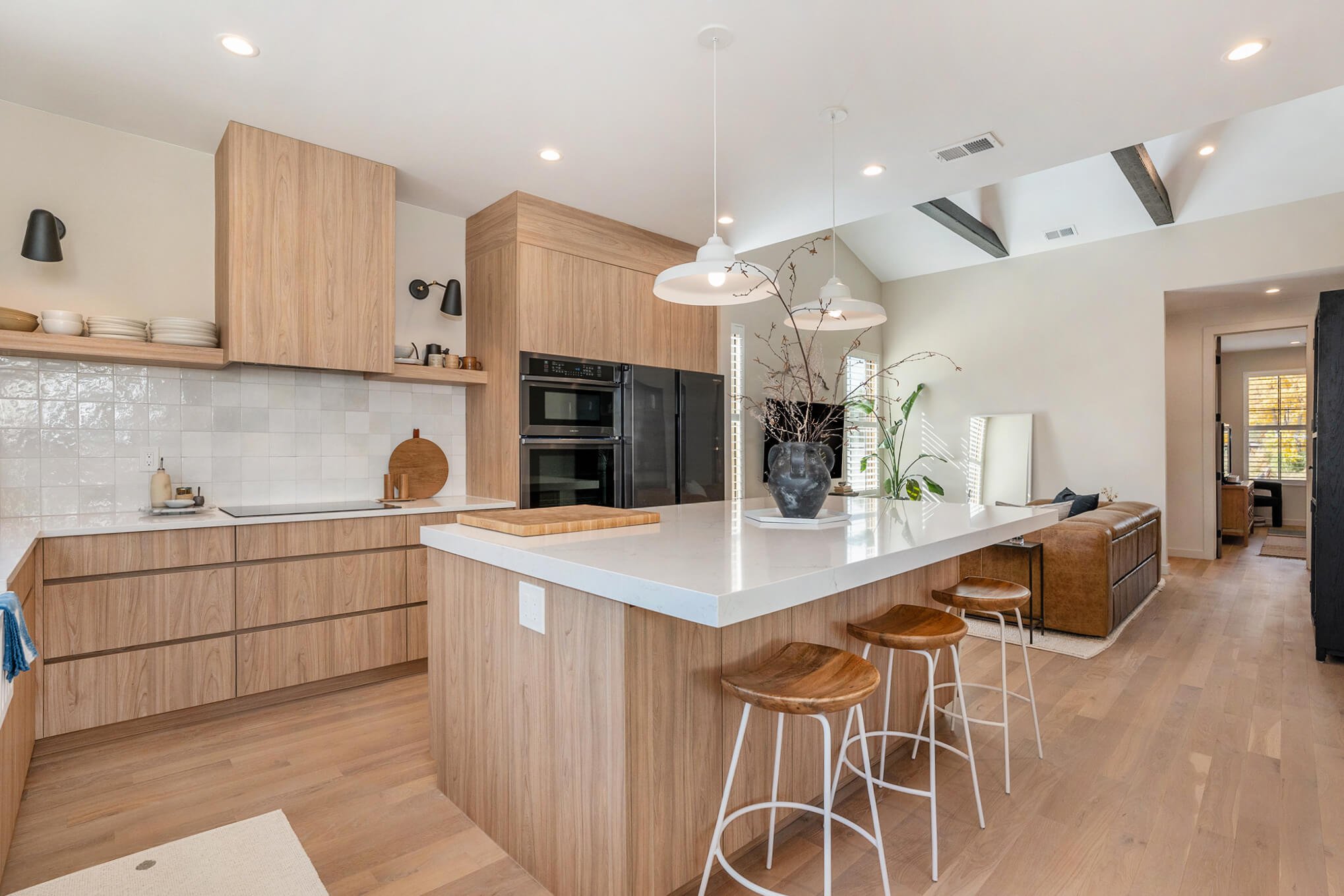 Modern kitchen with wood cabinets, white countertops, bar stools, and pendant lights.