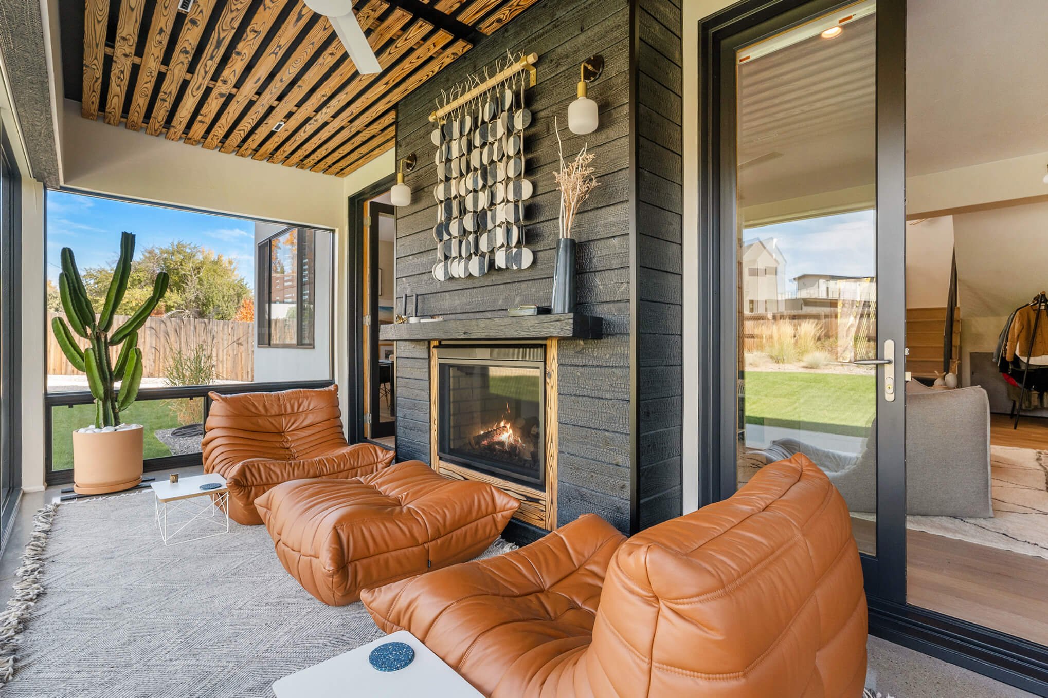 Modern living room with leather chairs, fireplace, large windows, ceiling fan, and potted cactus.