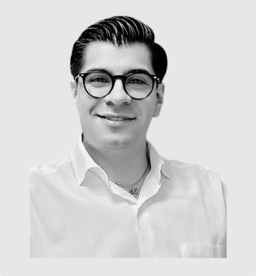 Retrato de un hombre sonriendo, con gafas y peinado peinado hacia atrás, vestimenta formal y fondo gris.