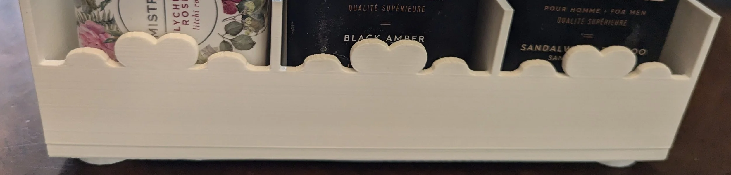 The front of a soap storage bin.  There is a white heart motif along the top, and the bin is sectioned into thirds, each third wide enough to hold an upright bar of soap.