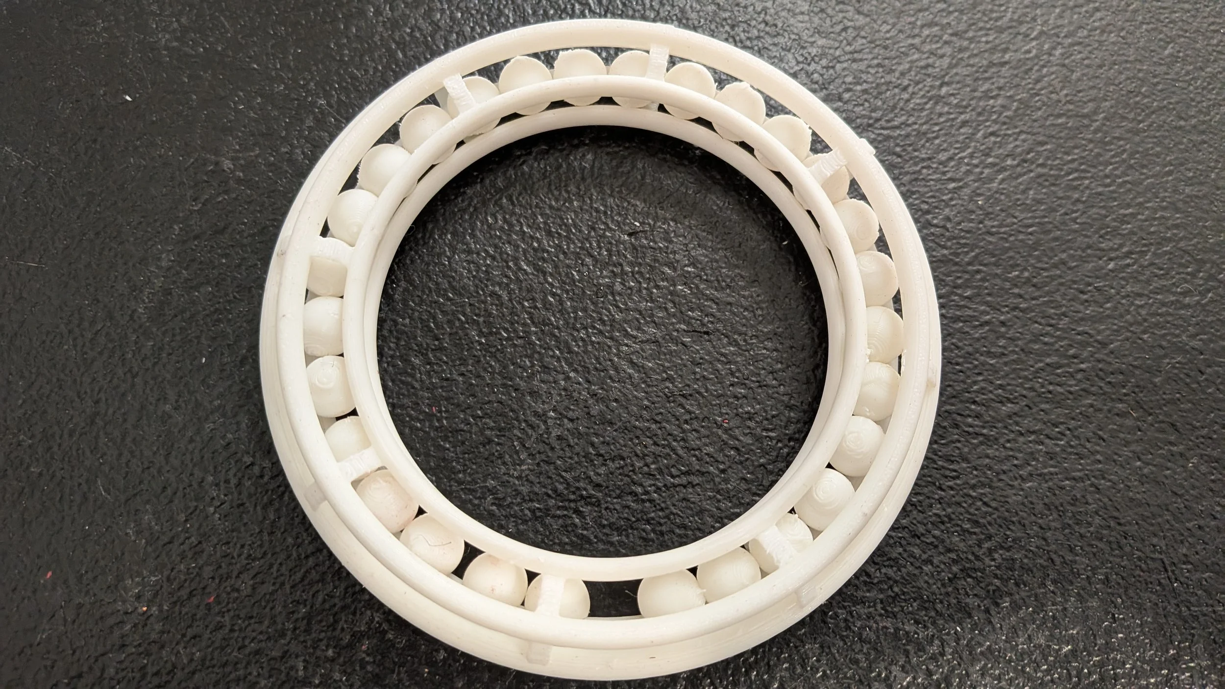 The finished beaded fidget bracelet has five rings caging an invisible torus.  The rings are held together with a series of clamps that are open on the inside.  The bracelet is full of beads.