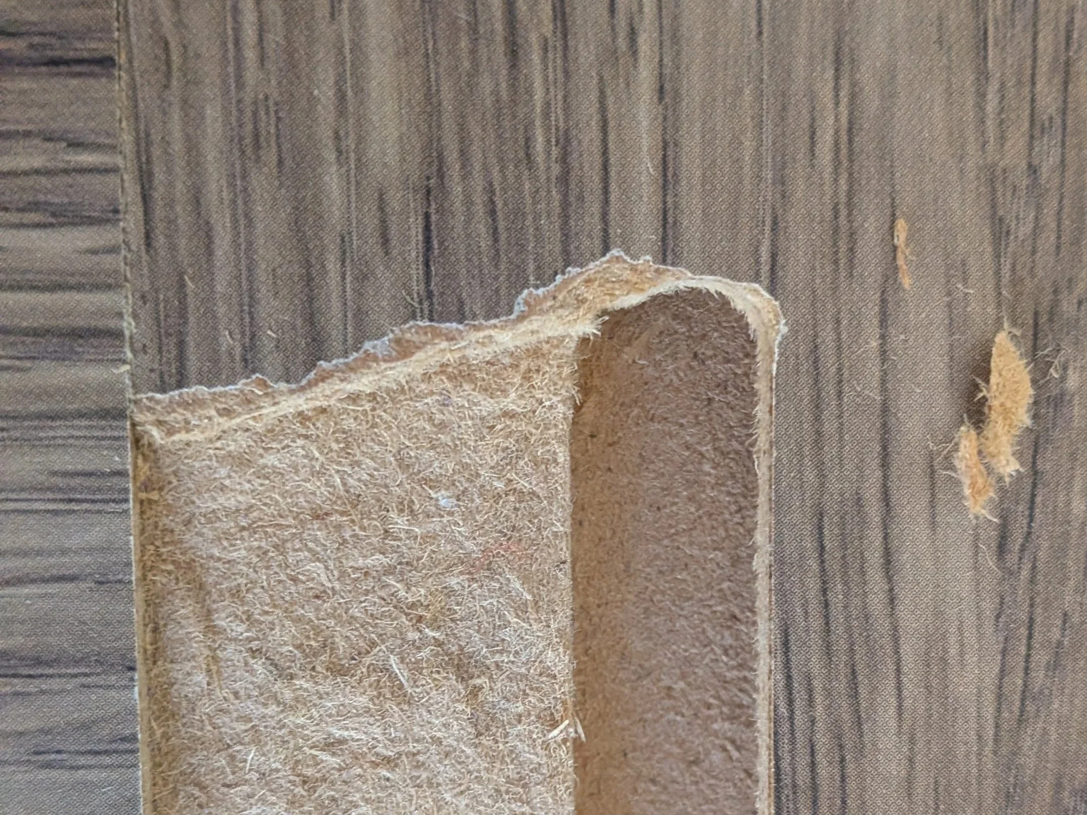 A broken piece of particle board furniture has a straight edge where it's been trimmed.