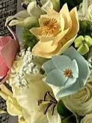 A close-up of three 3D printed magnolias in a wedding bouquet.  The magnolias are painted pink, buttery yellow, and pale blue.