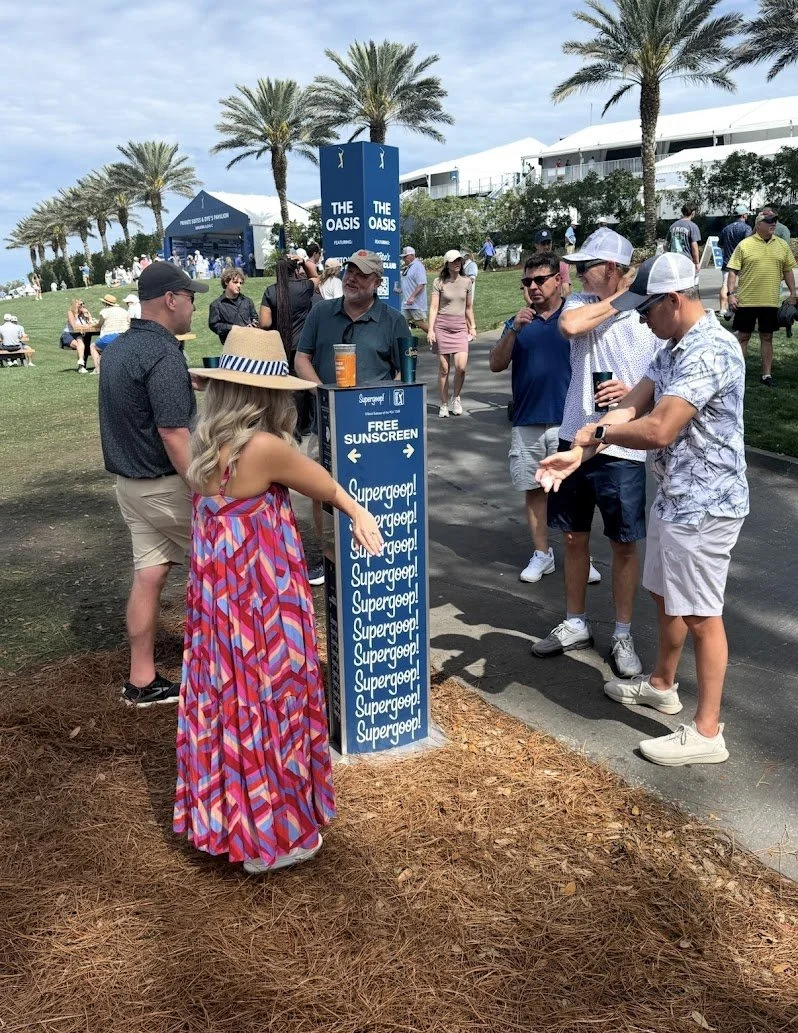 People surrounding a Supergoop branded sunscreen dispenser at THE PLAYERS Championship providing free sunscreen for fans at major outdoor sporting events.