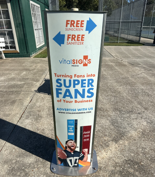 Outdoor smart kiosk offering free sunscreen and sanitizer, with arrows pointing left and right, and promoting turning fans into super fans for a business, with contact details and an image of a football player celebrating.