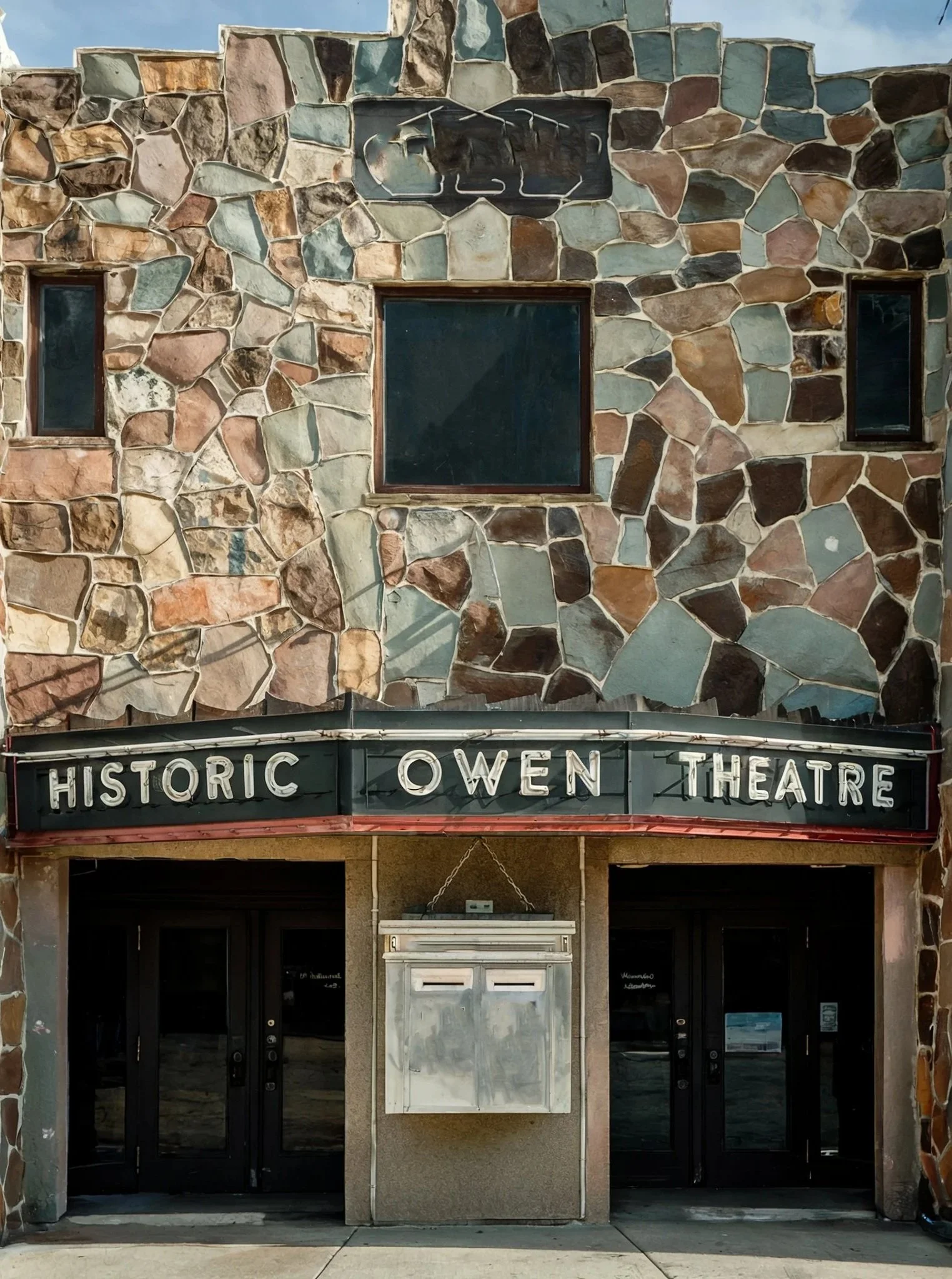 Facade of the Historic Owen Theatre with a stone wall, black marquee sign, and double glass doors.