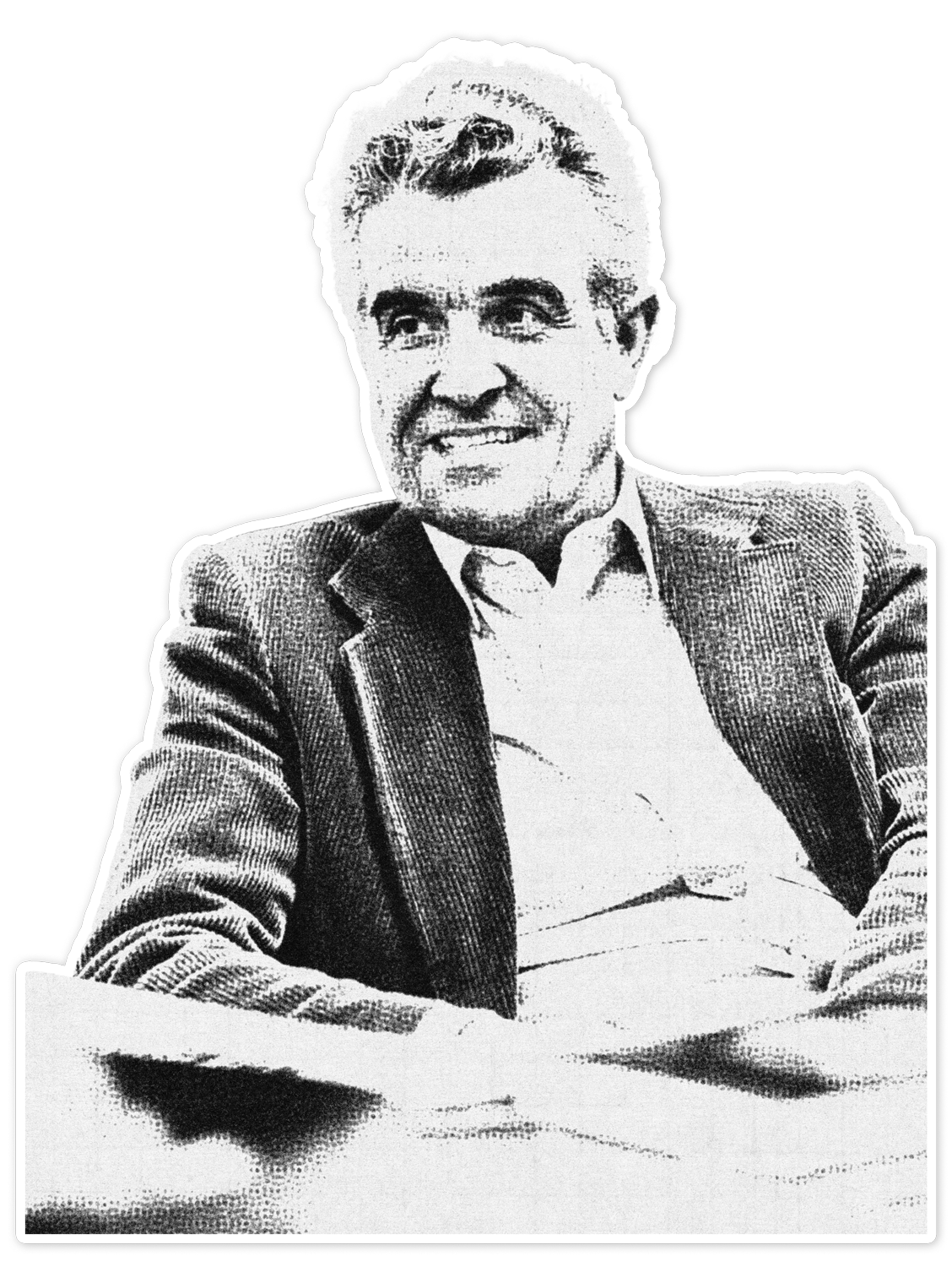 Black and white photo of a man sitting at a table, wearing a suit jacket and a collared shirt, smiling and looking slightly to the right.