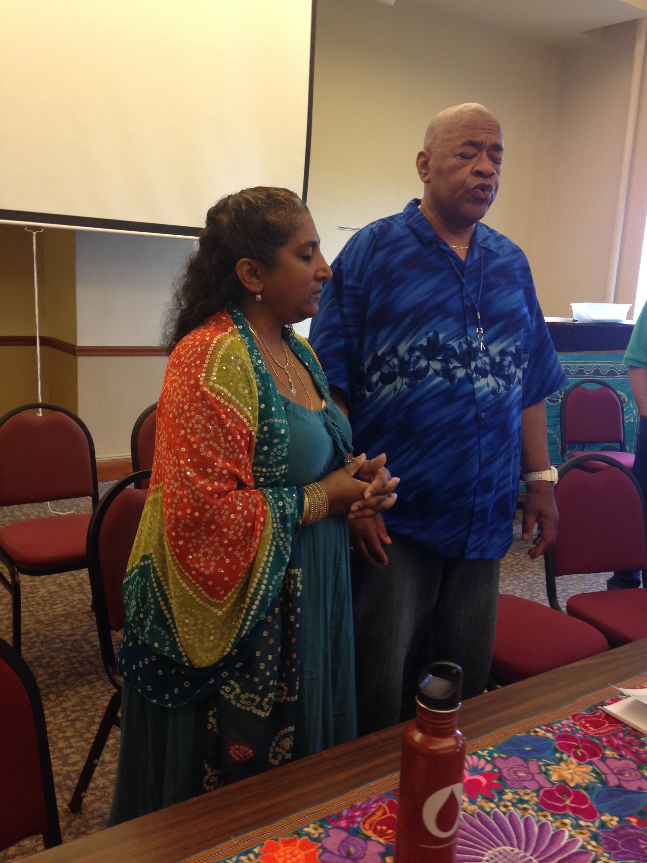 A woman and a man standing with eyes closed, leading conference participants in song.