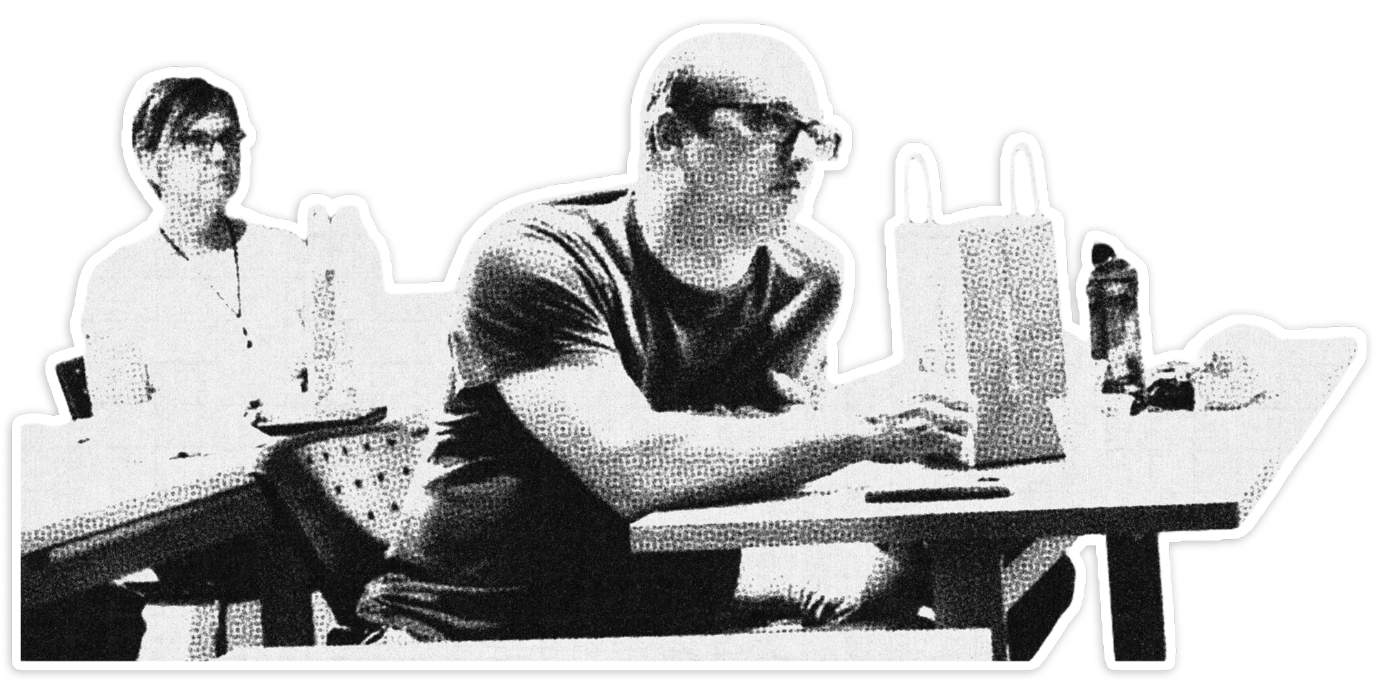 Two men sitting at a table with bottles and cups, one man is wearing glasses and a dark T-shirt, the other man is wearing a light T-shirt, both are looking at a laptop.