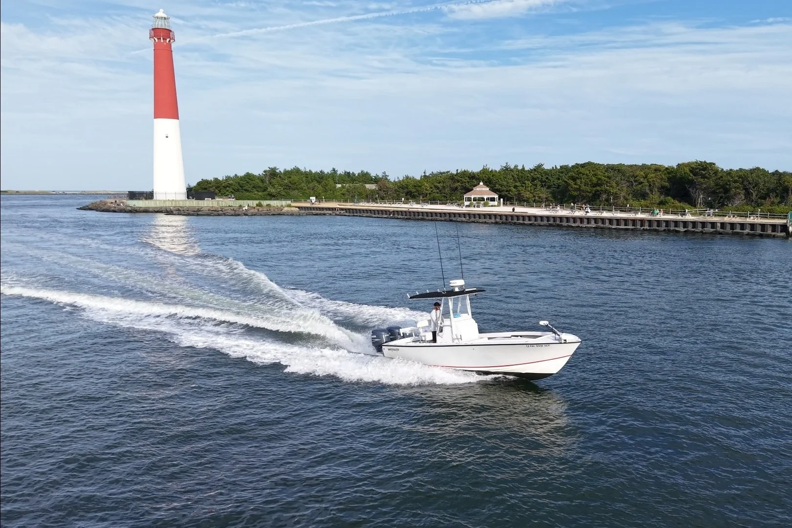 A Whitewater 25 cruises in Barnegat Inlet in front of the lighthouse Barnegat Light on Barnegat Bay ready to go fishing or on sunset cruise or bay cruise. The charter captain is driving the center console near Long Beach Island or LBI in New Jersey