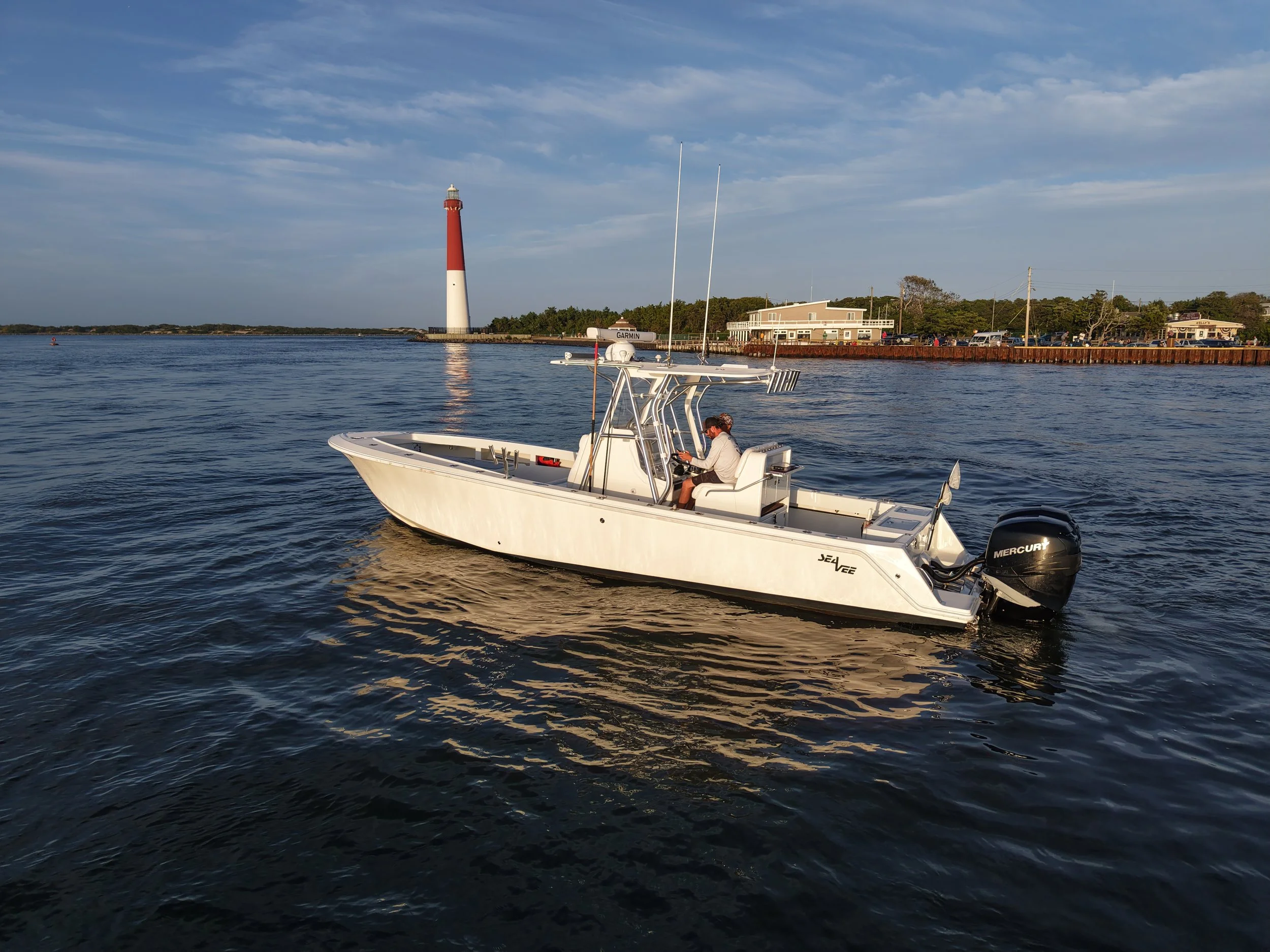 A Seavee 320B sits in Barnegat Inlet in front of the lighthouse Barnegat Light on Barnegat Bay ready to go fishing or on sunset cruise or bay cruise. The charter captain is driving the center console near Long Beach Island or LBI in New Jersey