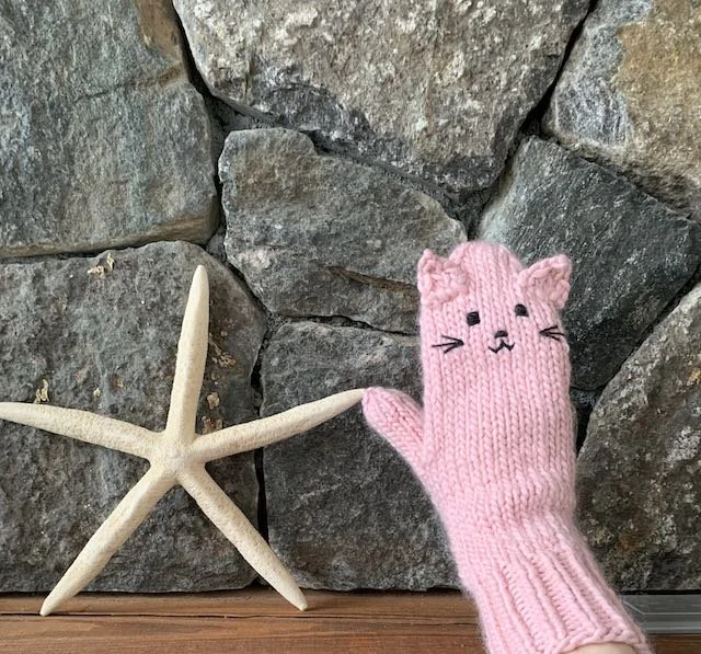 A pink cat-shaped mitten with the thumb touching a starfish against a stone wall.