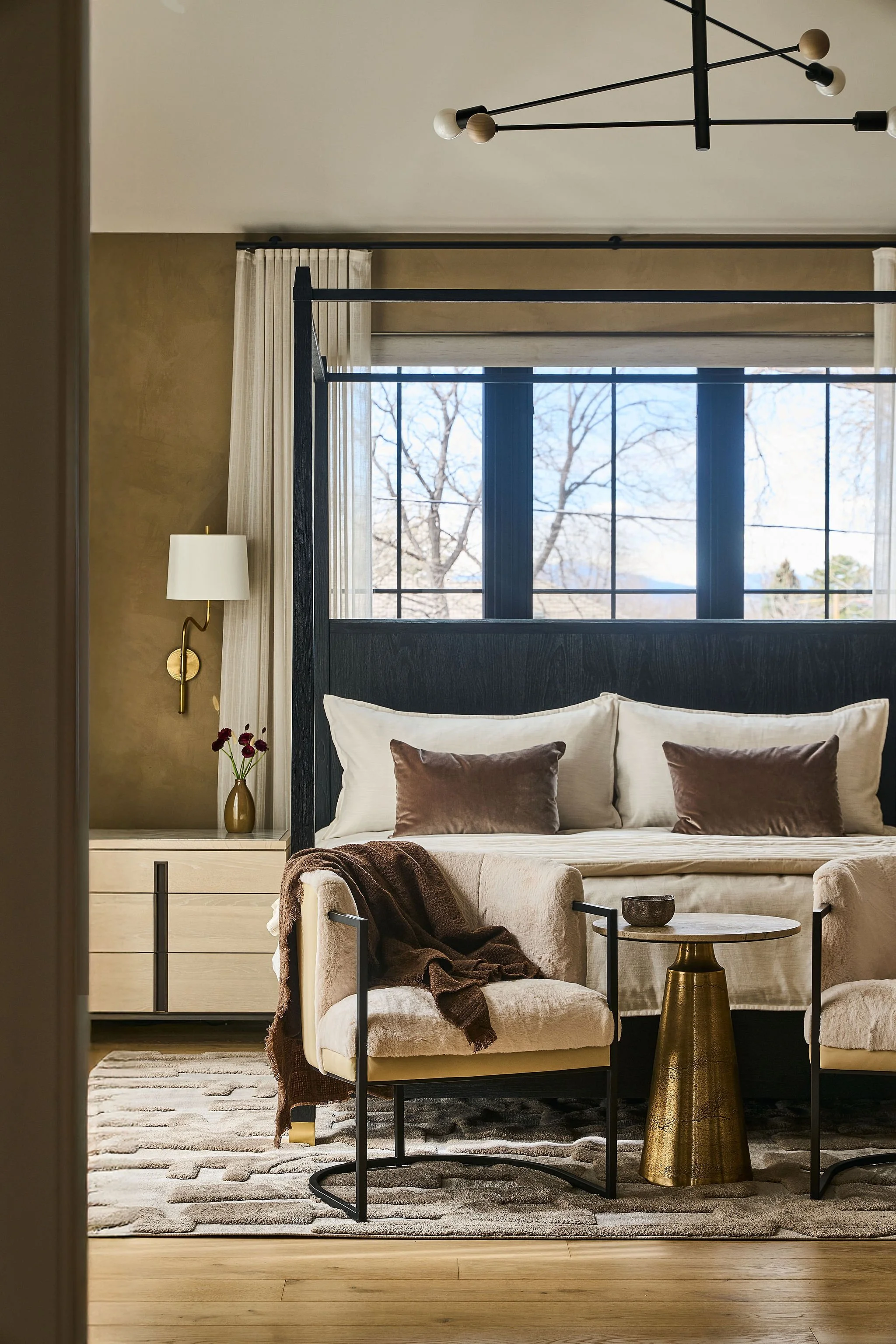 Warm, neutral primary bedroom with 4 poster bed & cozy fur chairs