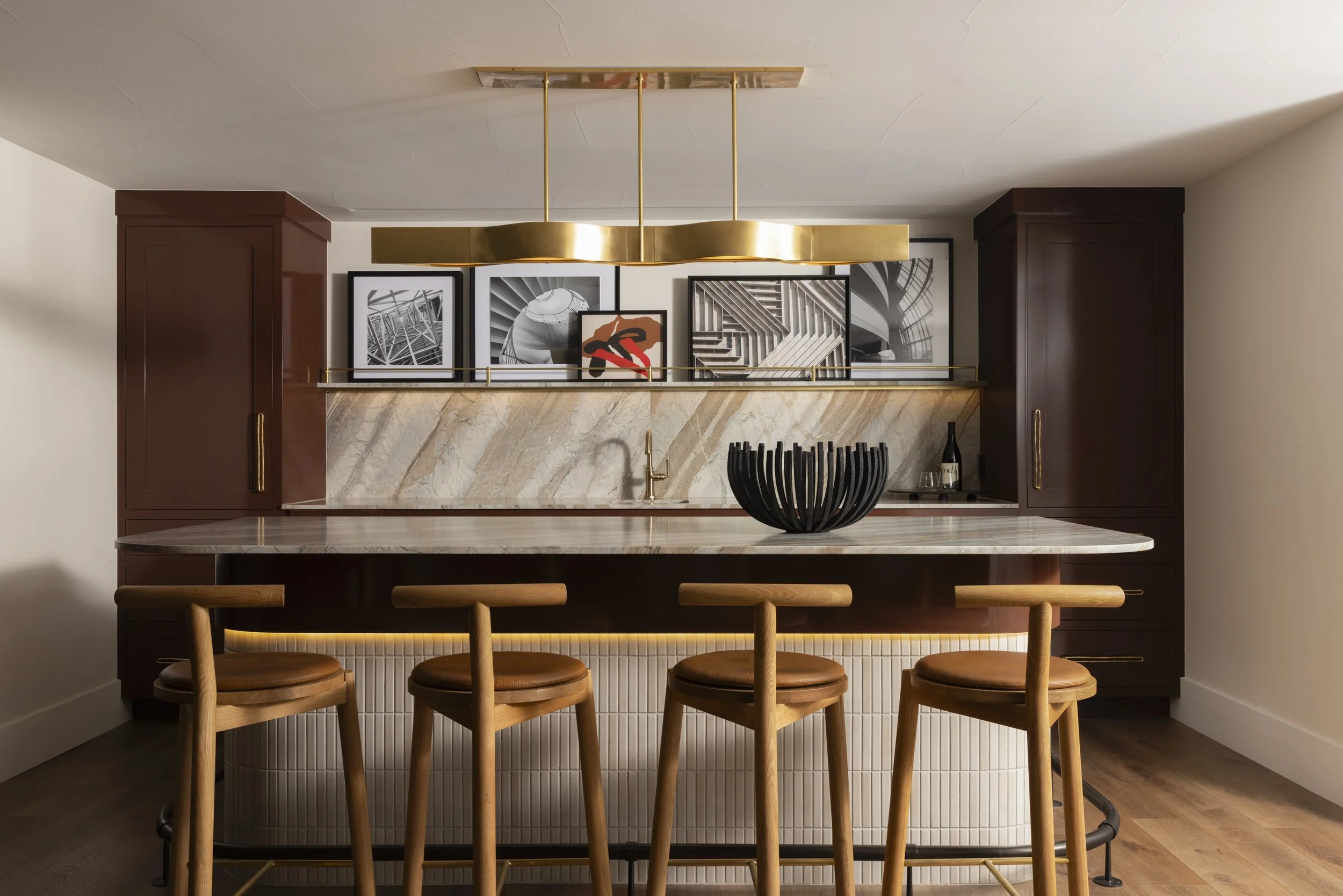 Custom basement bar with warm wood cabinetry, stone backsplash, and brass lighting in Boulder remodel