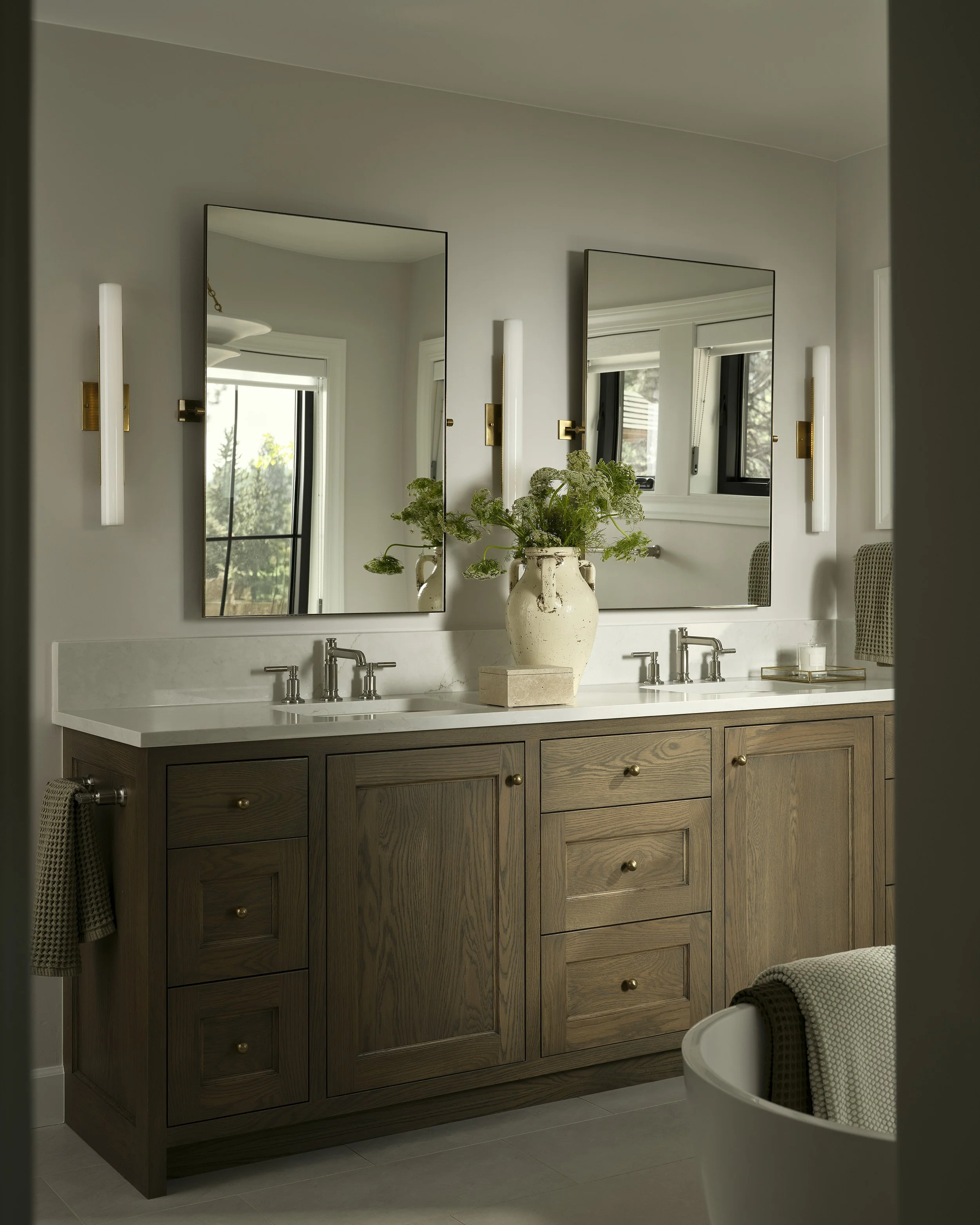 Double vanity with warm wood cabinetry and modern sconces in Denver primary bathroom remodel