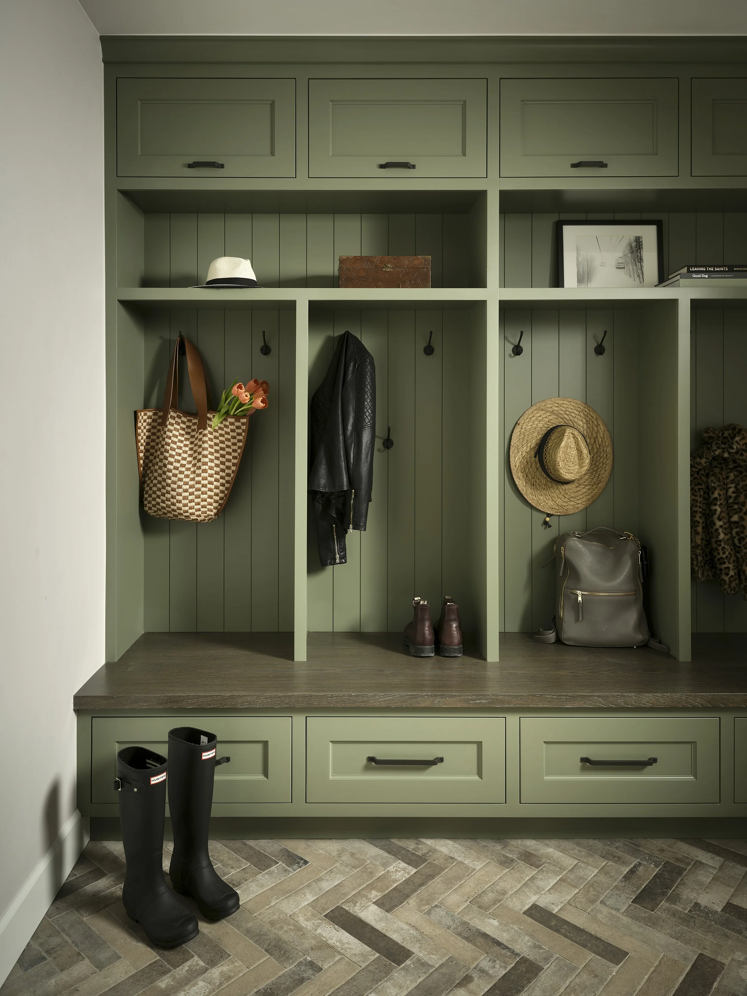 Custom green mudroom cabinetry with built-in storage and herringbone brick flooring