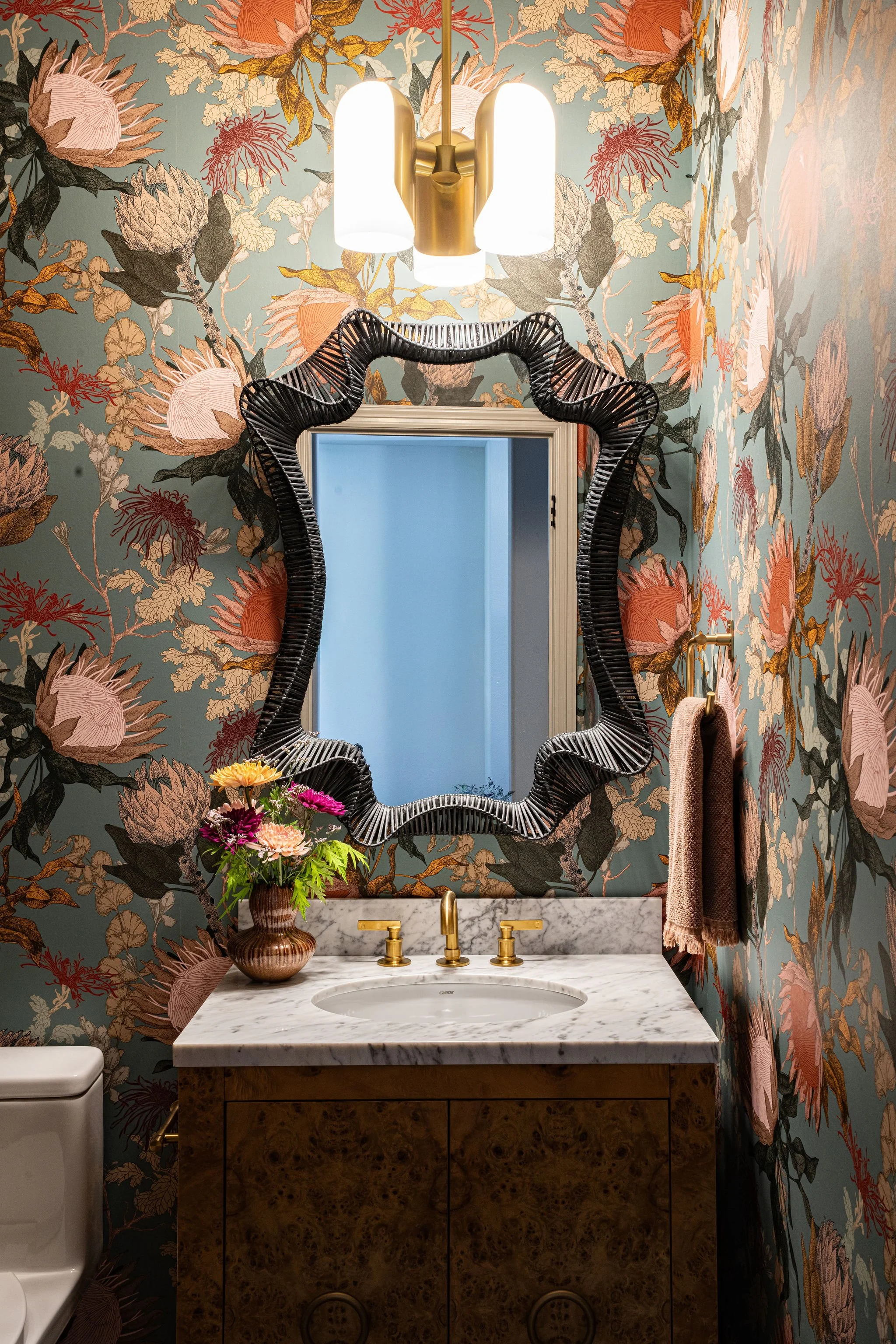 floral wallpaper powder bath with brass faucet and rattan mirror
