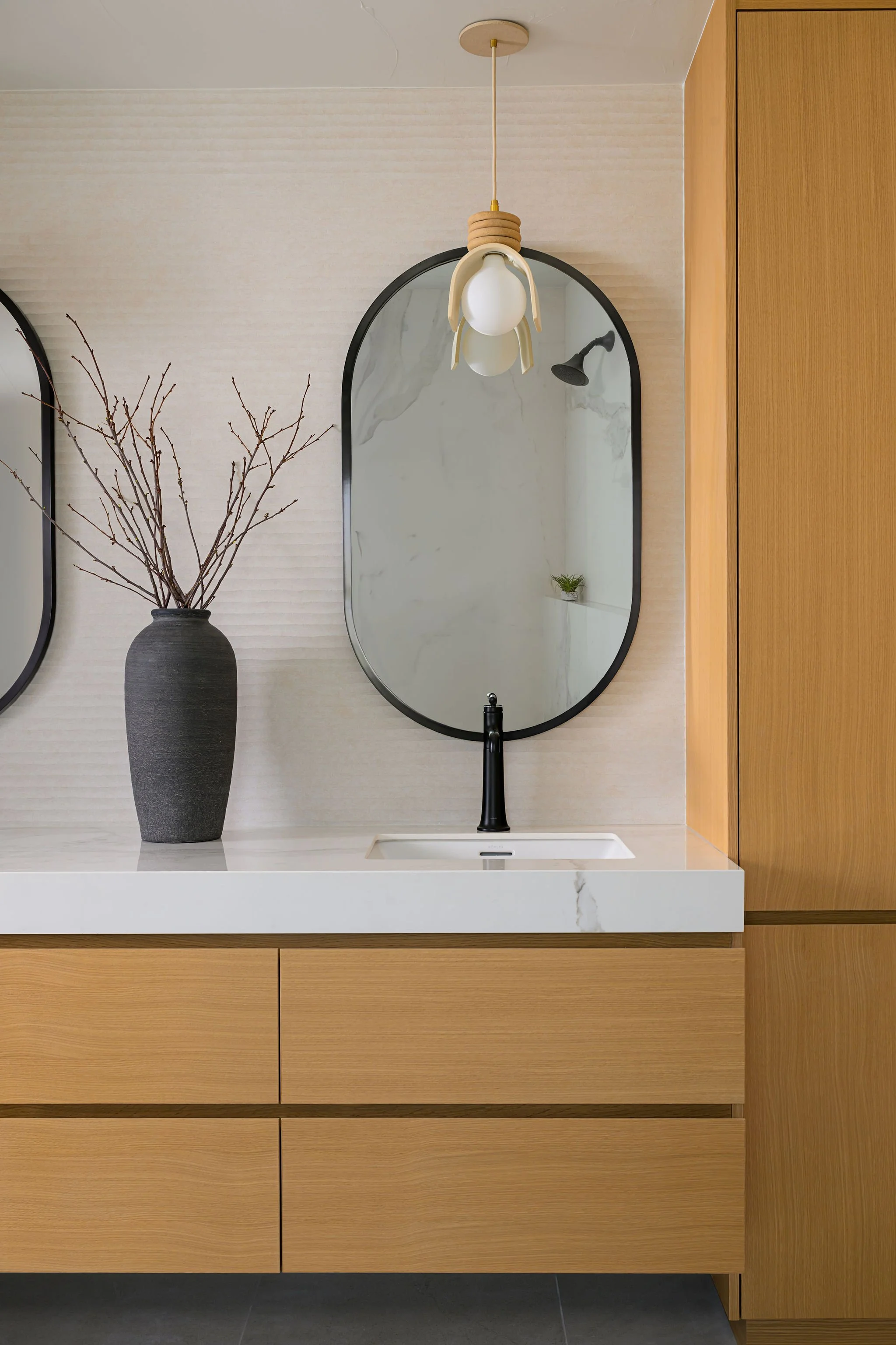 Modern primary bathroom vanity with white oak cabinetry and oval mirror detail
