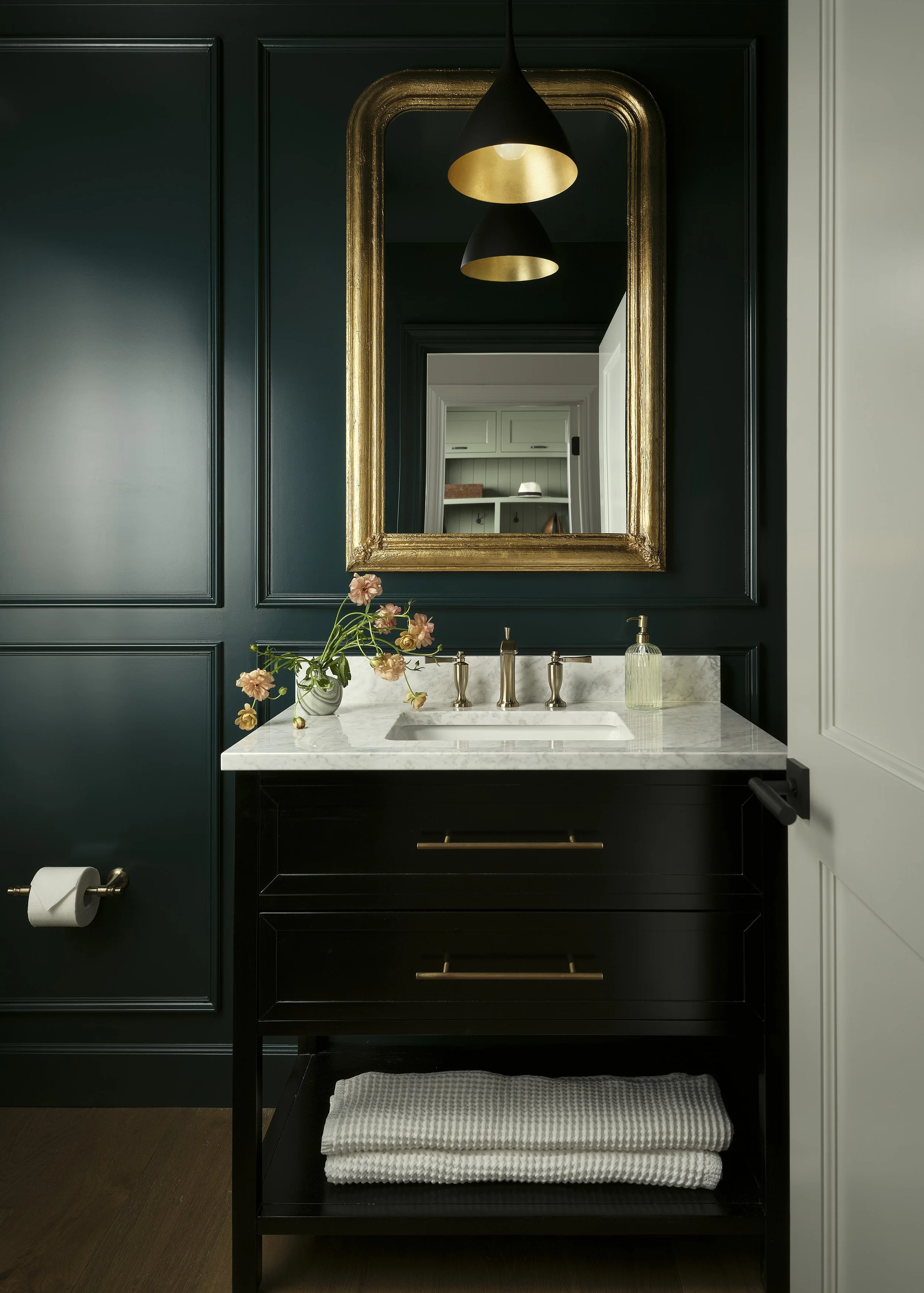 Moody powder bathroom with dark paneling, brass mirror, and marble vanity