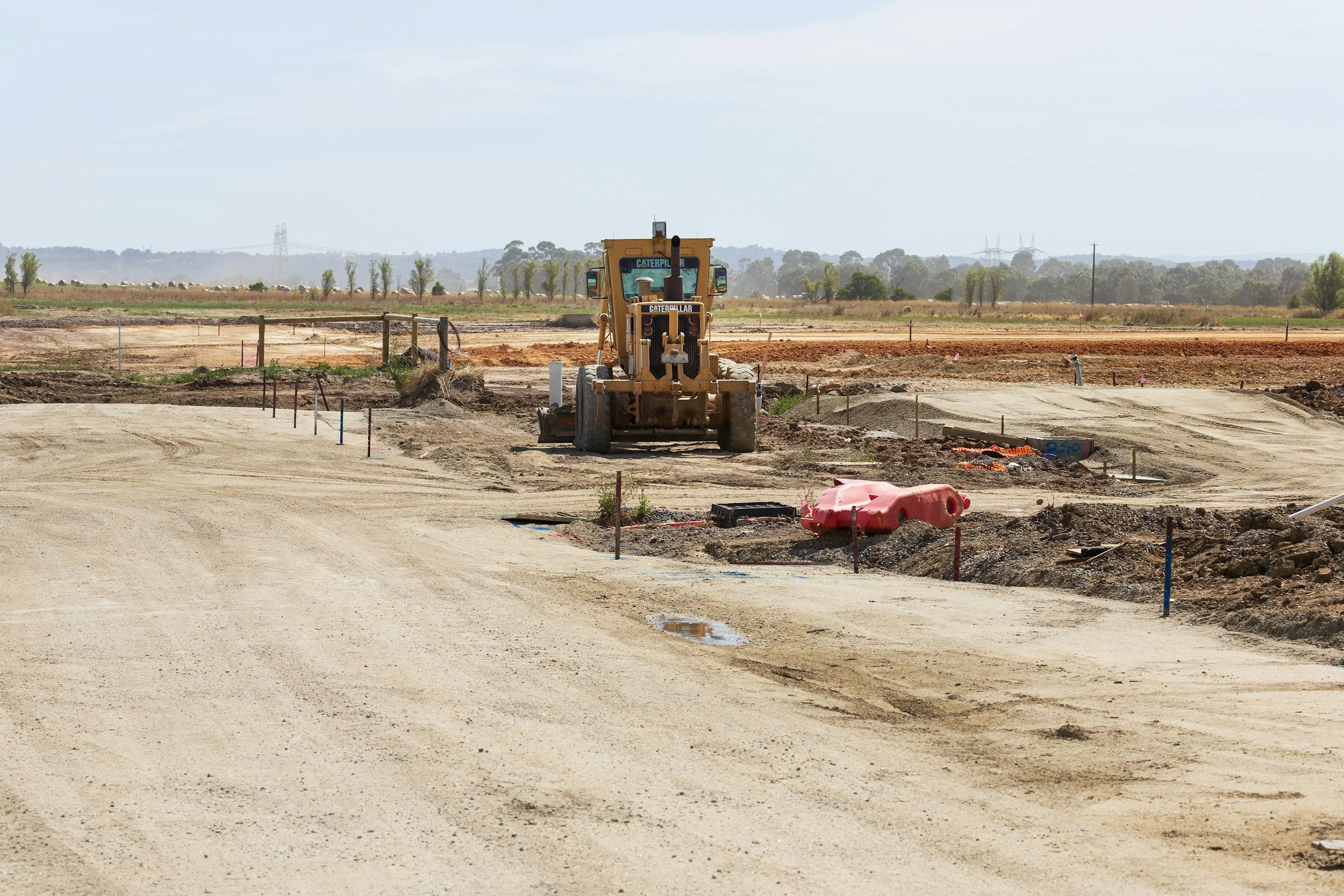 Silhouette of a construction worker wearing a helmet, leaning over, and working on a metal fence against a partly cloudy sky, building a Fathom Tanks water simulation tank.