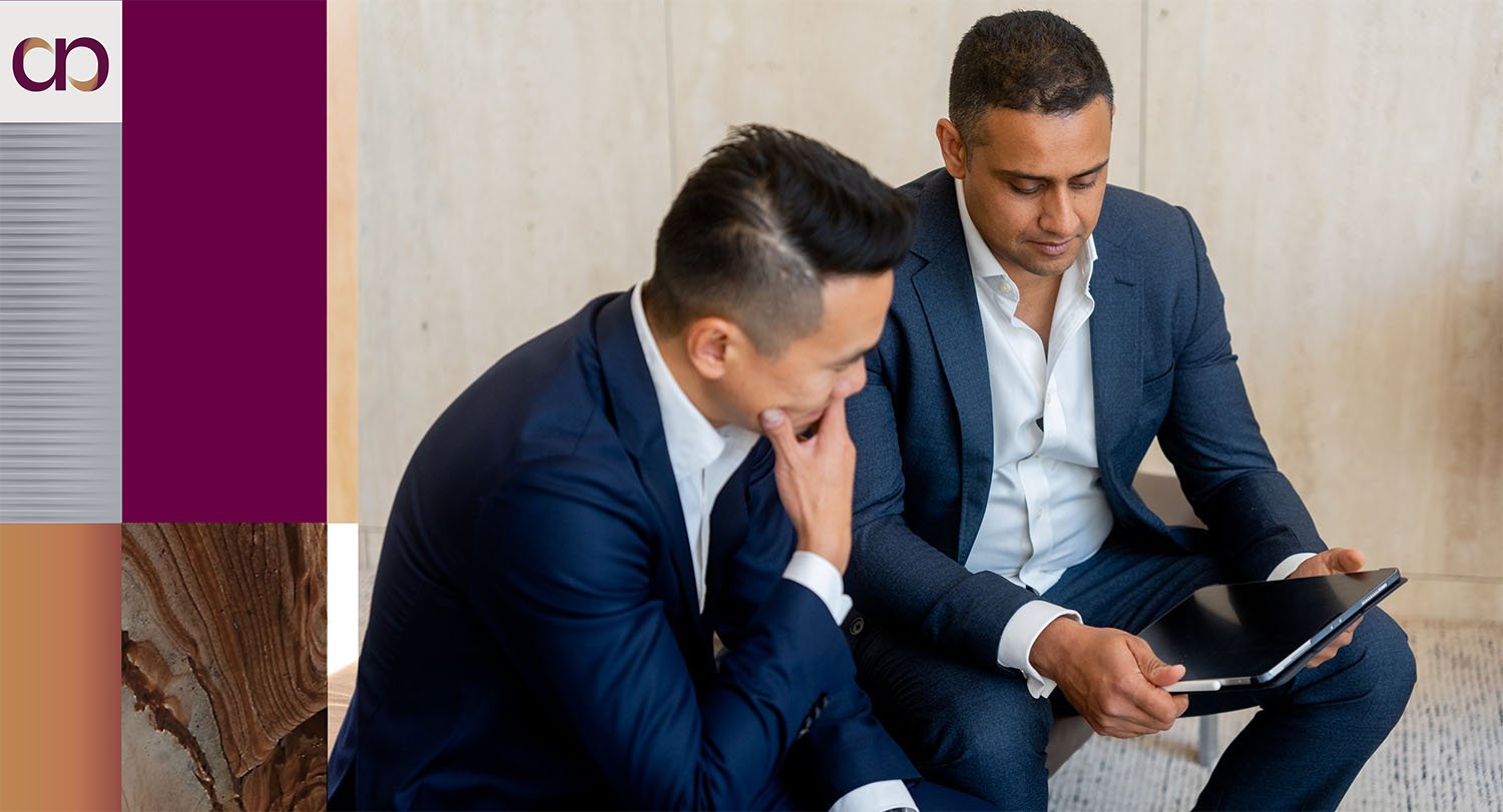 Abundant Financial Advisory founders Timothy Lee and Simran Dhillon in suits looking at a shared tablet