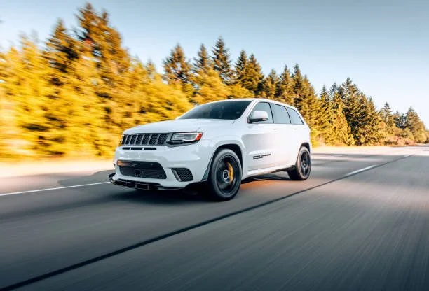 A white SUV driving on an open highway with trees in the background during daylight.