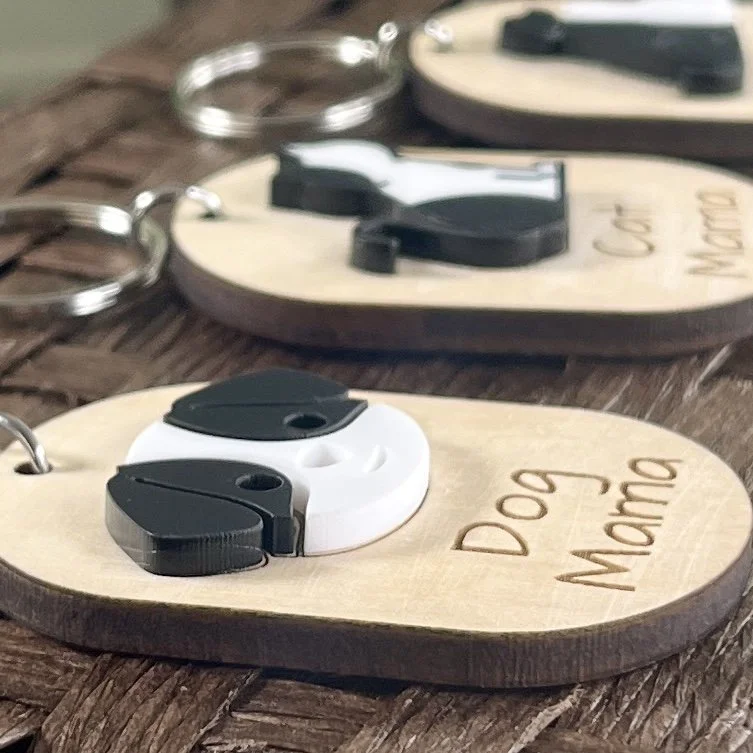 side view of laser cut maple wood keychain displaying a raised black/white acrylic dog face and engraved "Dog Mama" to highlight  depth and texture.
