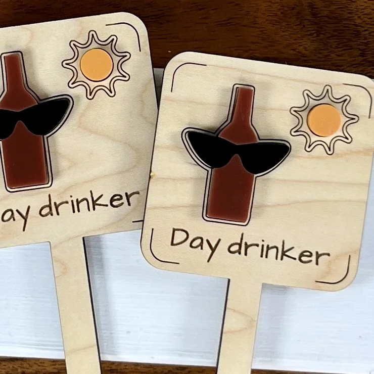 flat lay maple plant stake featuring layered acrylic bottle, sunglasses and sun embellishments engraved with the phrase "Day Drinker".