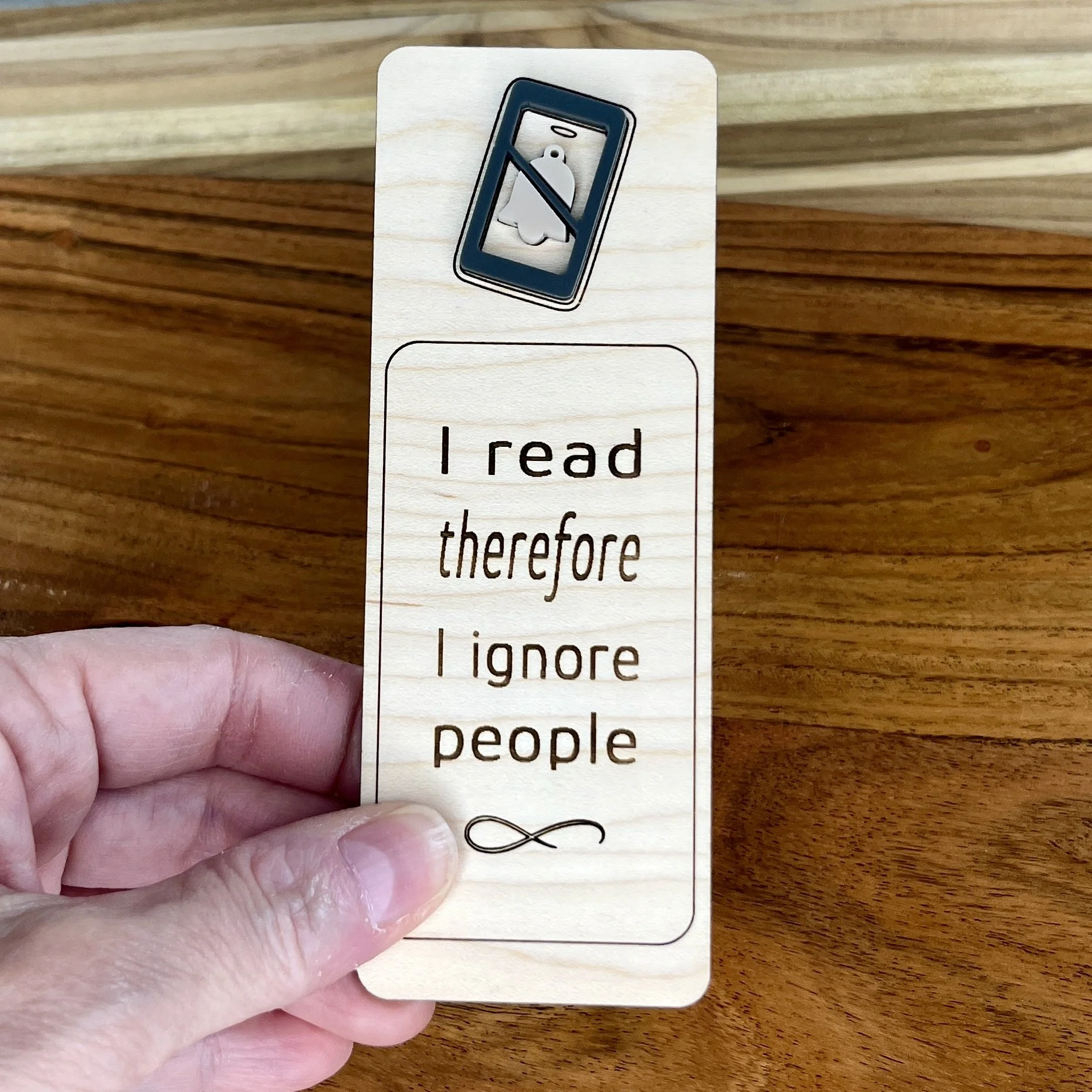 handheld maple bookmark featuring a blue acrylic do not disturb symbol embellishment engraved with the phrase "I read therefore I ignore people".