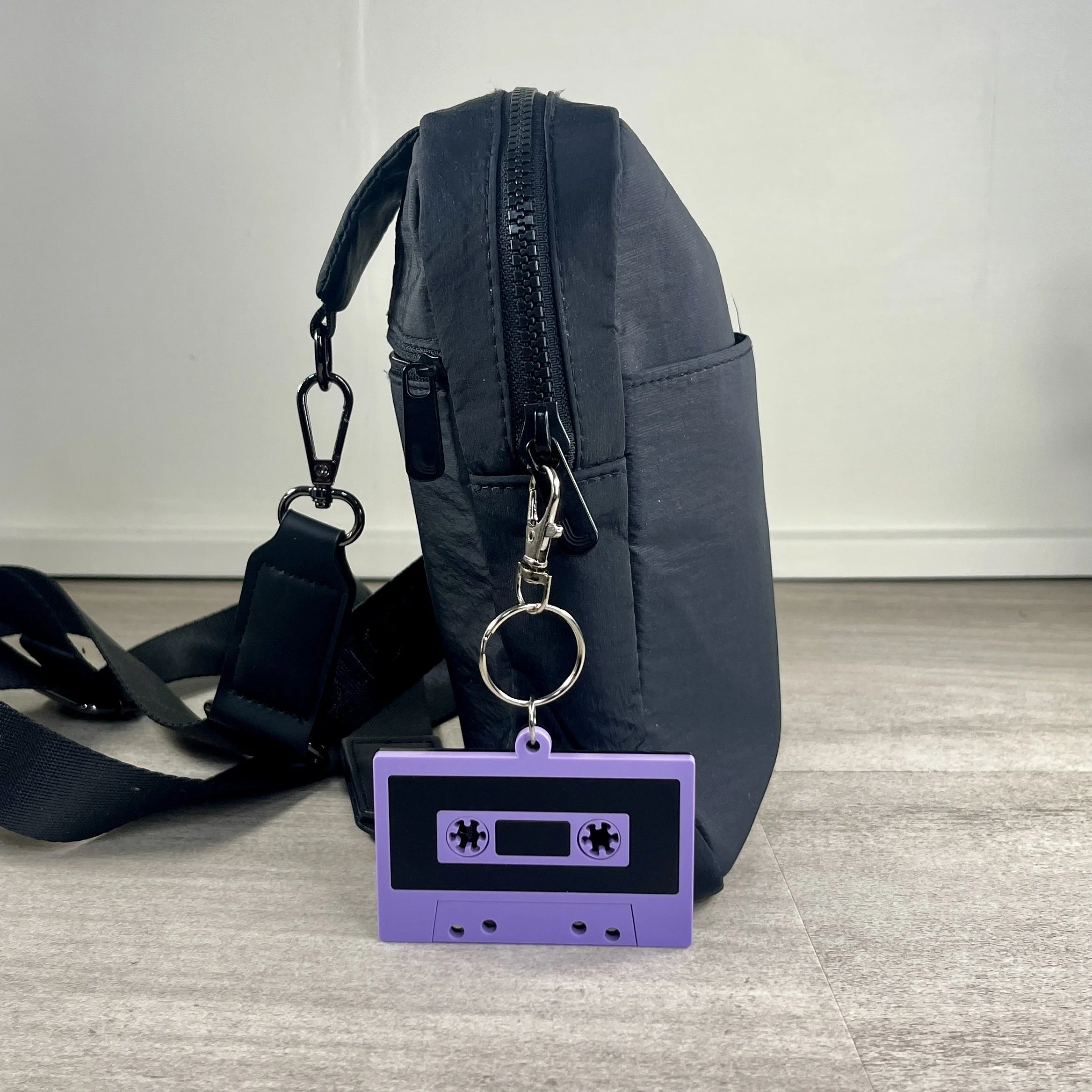 Retro cassette tape-shaped acrylic backpack tag in use, hanging from a bag.