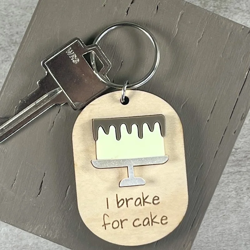 lifestyle shot of laser cut maple wood keychain featuring raised matte acrylic iced layer cake on a platter and engraved with the phrase "I brake for cake".