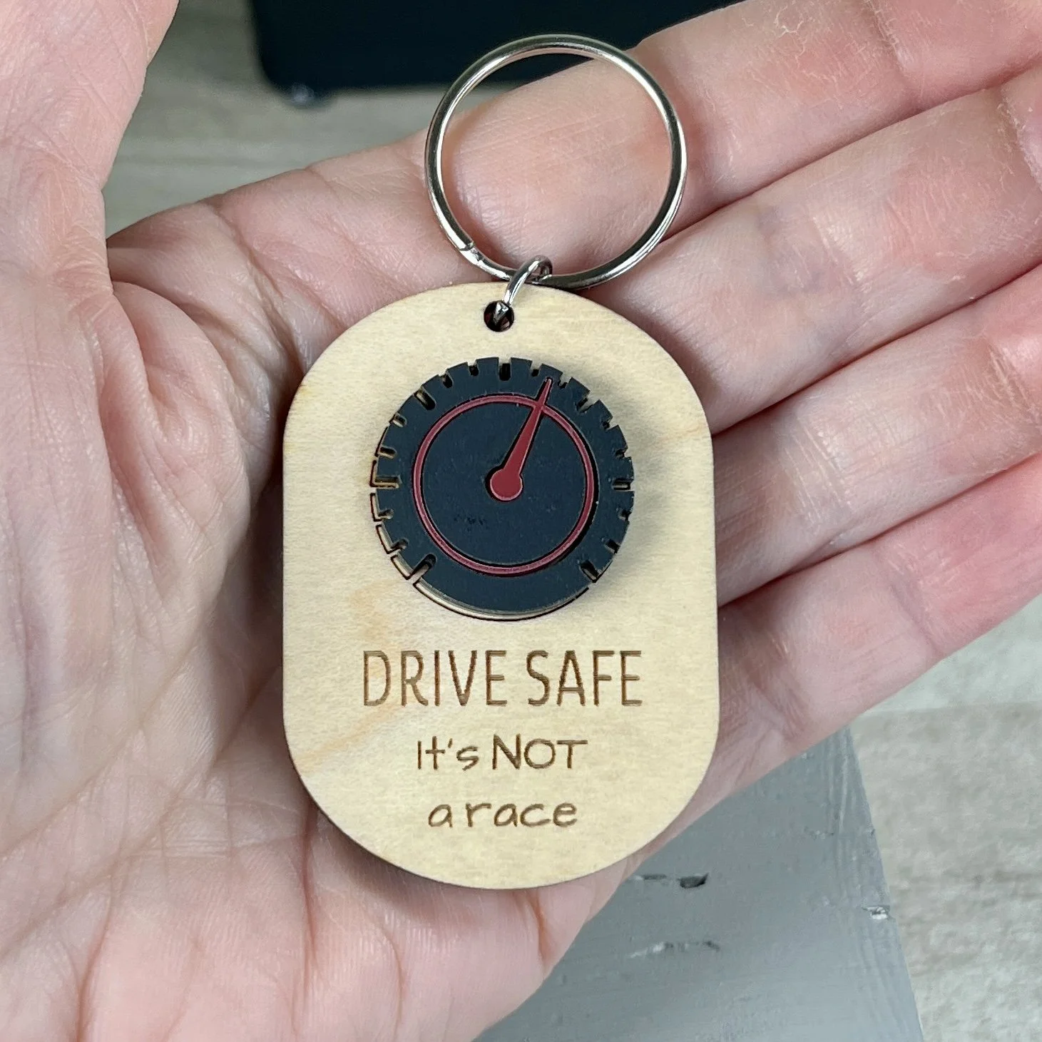 handheld laser cut maple wood keychain with speedometer in matte black/red acrylic and the engraved phrase "DRIVE SAFE It's not a race".