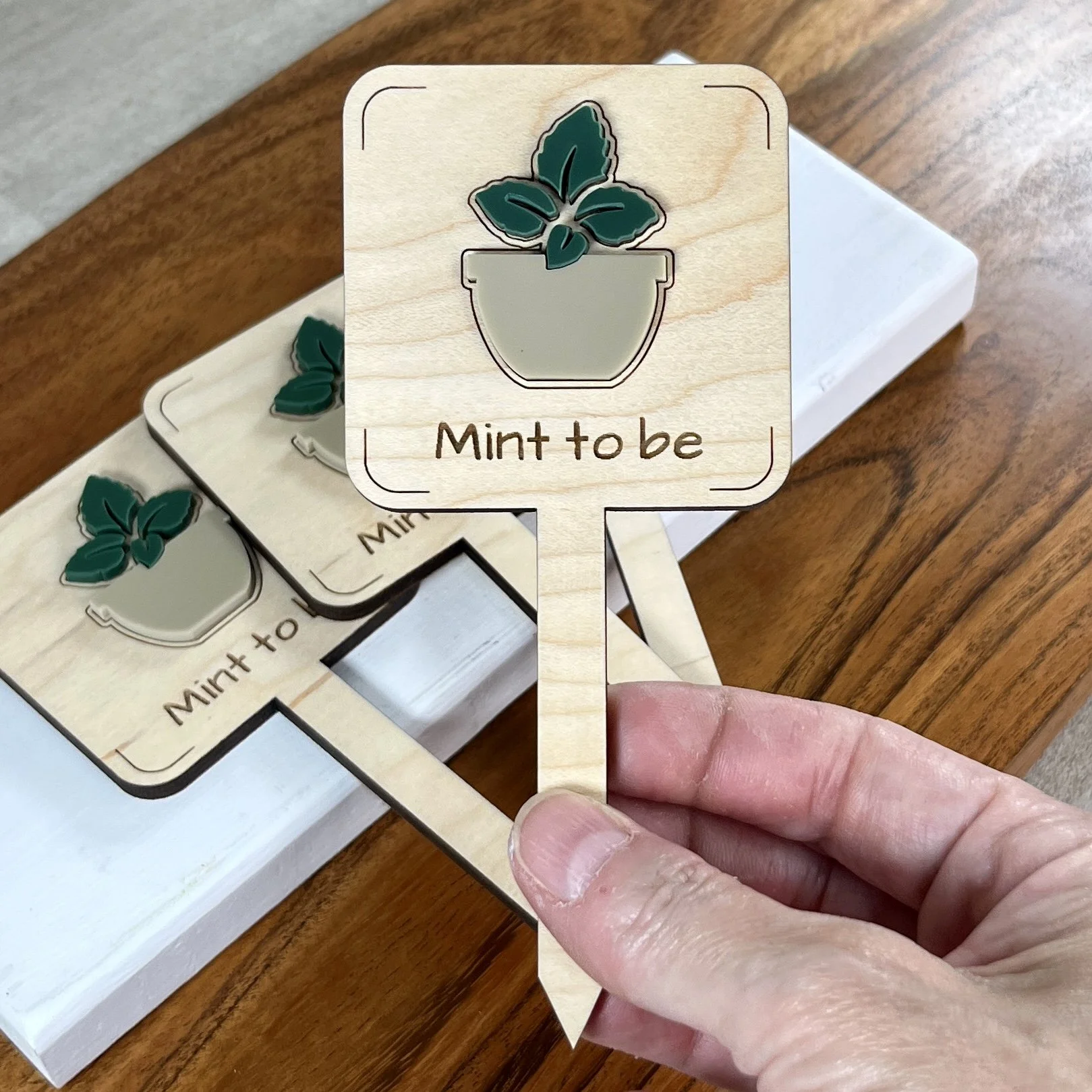 handheld maple plant stake featuring a potted mint plant embellishment engraved with the phrase "Mint to be".