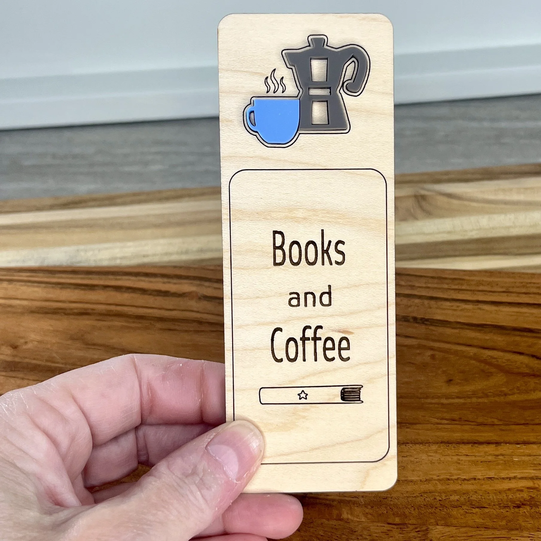 handheld maple bookmark featuring blue acrylic coffee cup and stovetop coffee pot embellishment engraved with the phrase "Books and Coffee".