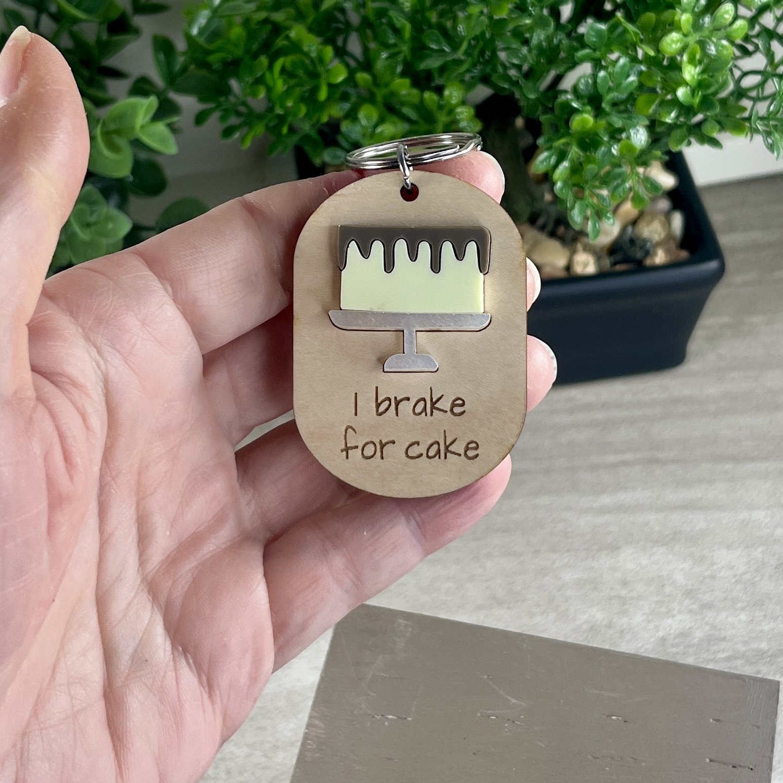 handheld laser cut maple wood keychain featuring raised matte acrylic iced layer cake on a platter and engraved with the phrase "I brake for cake".