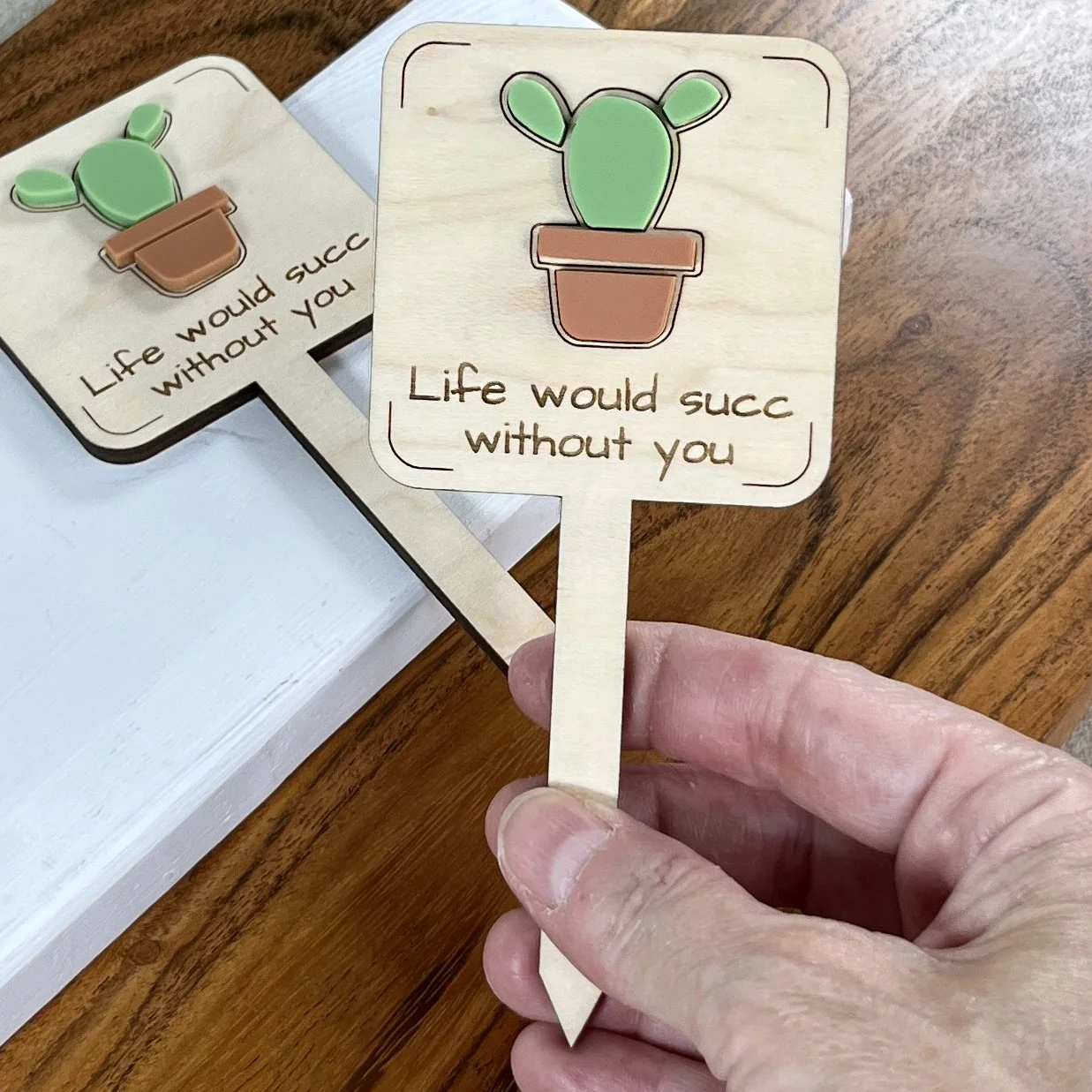 handheld maple plant stake featuring a potted succulent embellishment engraved with the phrase "Life would succ without you".