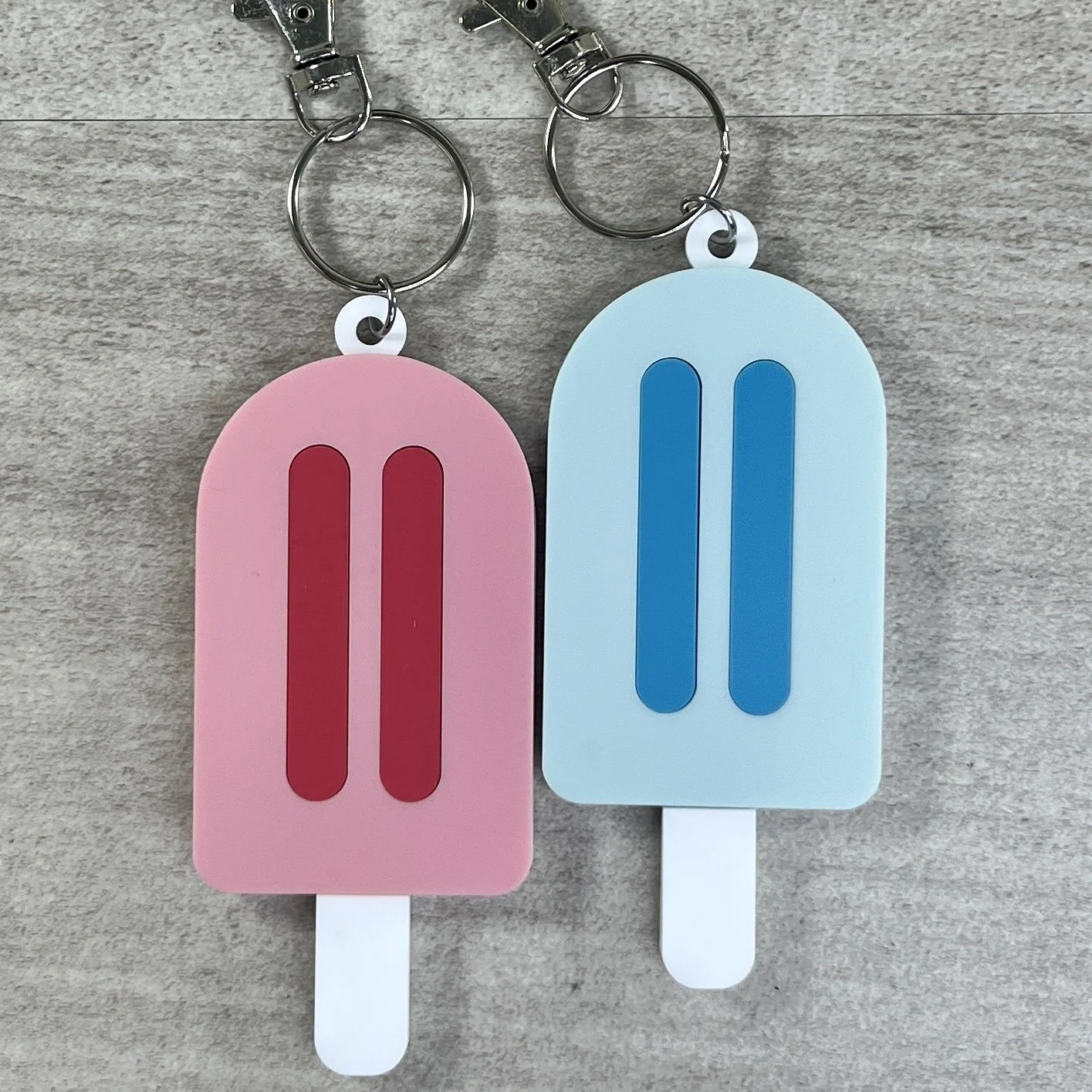 Set of two popsicle-shaped acrylic backpack tags in pink and blue.