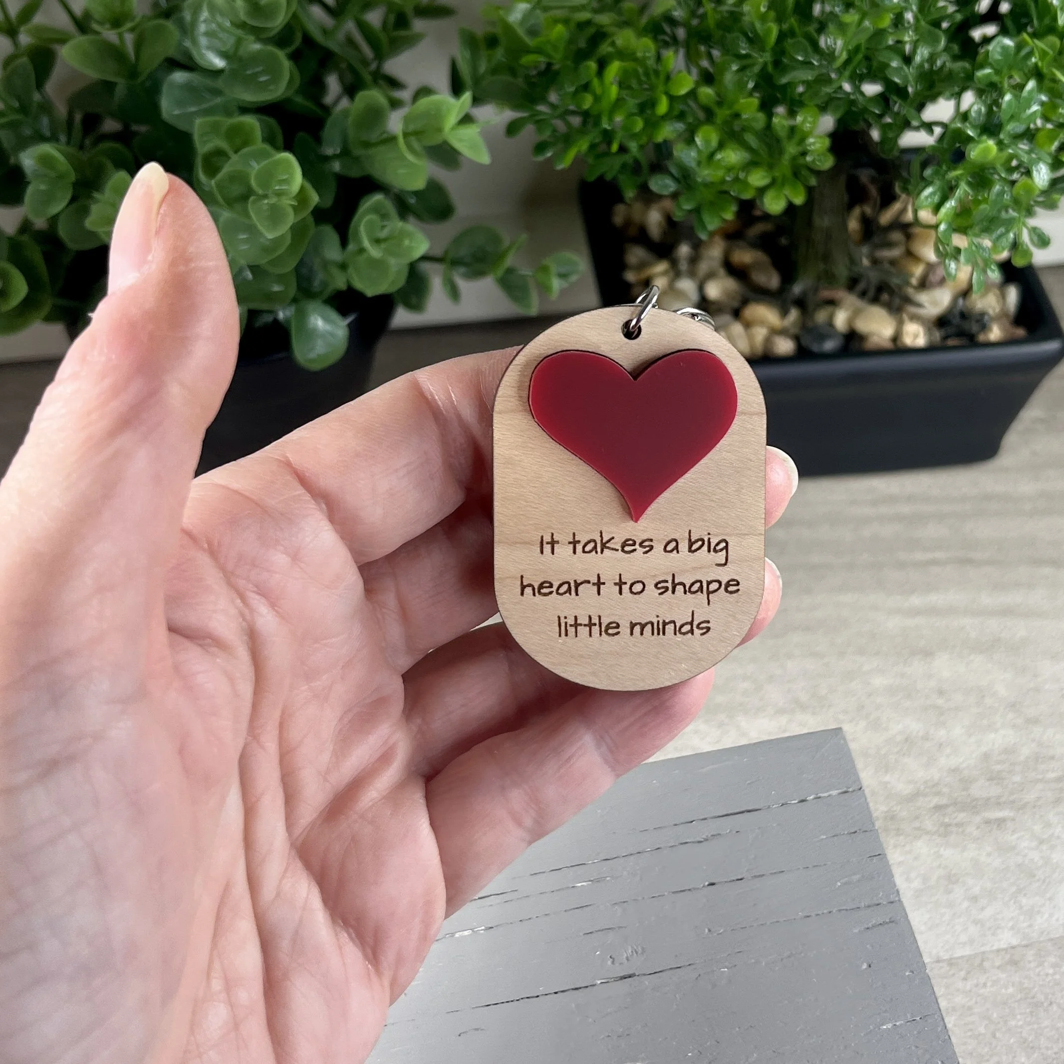 handheld laser cut maple wood keychain featuring raised matte red acrylic heart and engraved with the phrase "It takes a big heart to shape little minds".