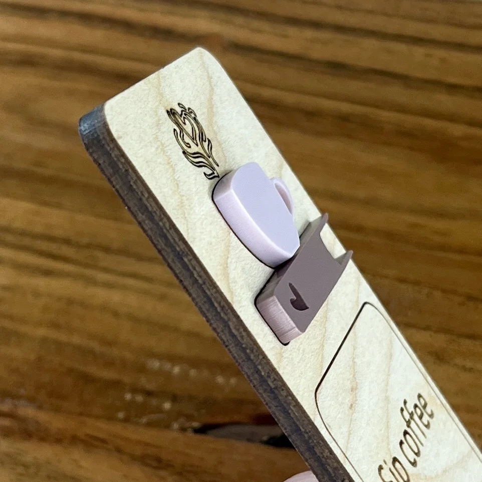 angled view maple bookmark featuring an ash rose coffee cup and mauve book embellishment engraved with the phrase "Sip coffee Read books Stay cozy".