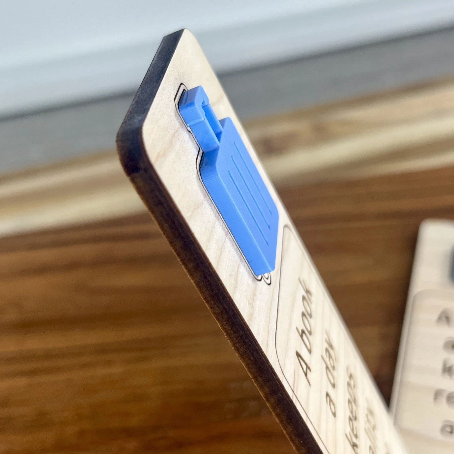 angled view maple wood bookmark with layered blue acrylic suitcase detail and engraved reader quote "A book a day keeps reality away".