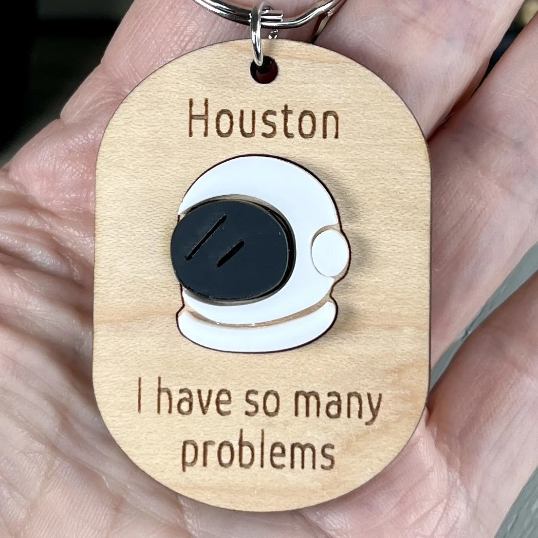 handheld laser cut maple keychain showing astronaut helmet graphic in raised matte white/black acrylic and engraved with "Houston I have so many problems".